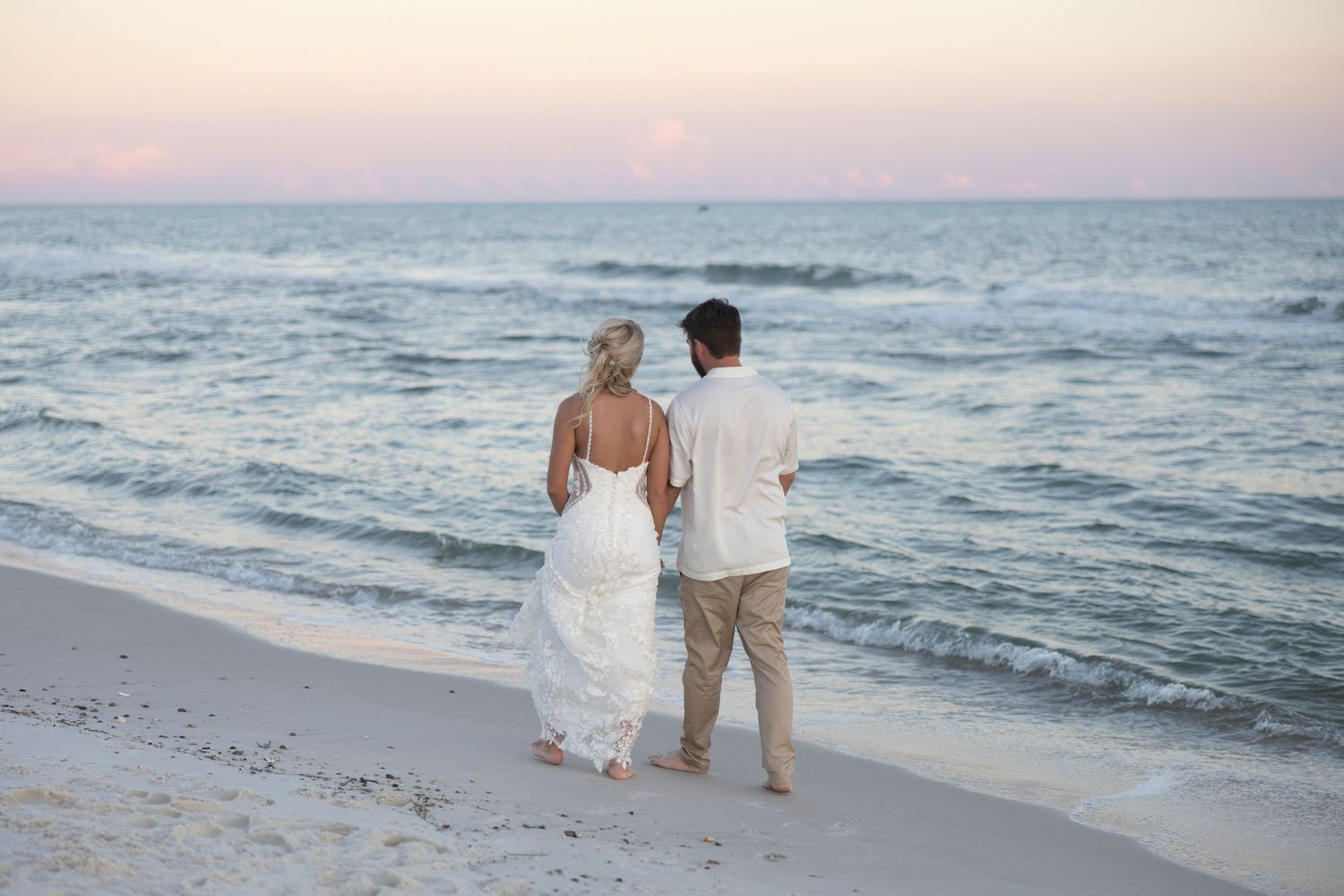 A couple walks along a scenic beach at sunset with gentle waves rolling onto the shore.