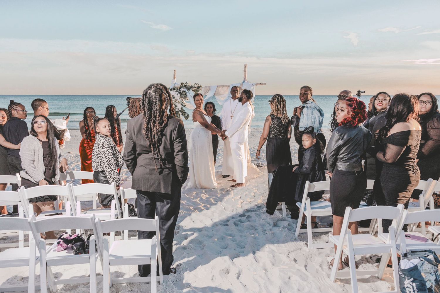 Wedding guests gather on a snowy beach with white chairs arranged for an outdoor winter ceremony.