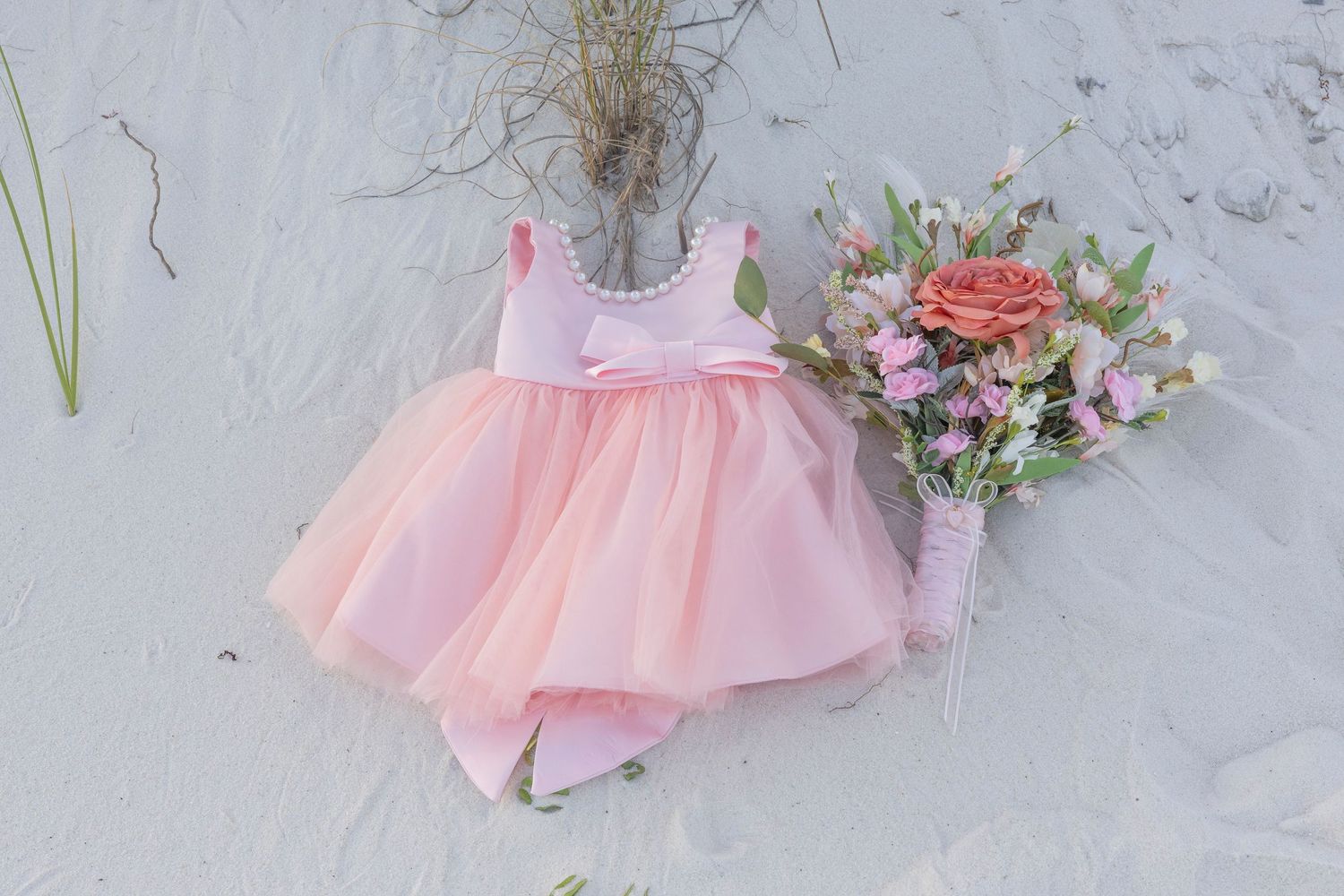 A pink tulle dress with floral details hangs delicately against a white textured wall.