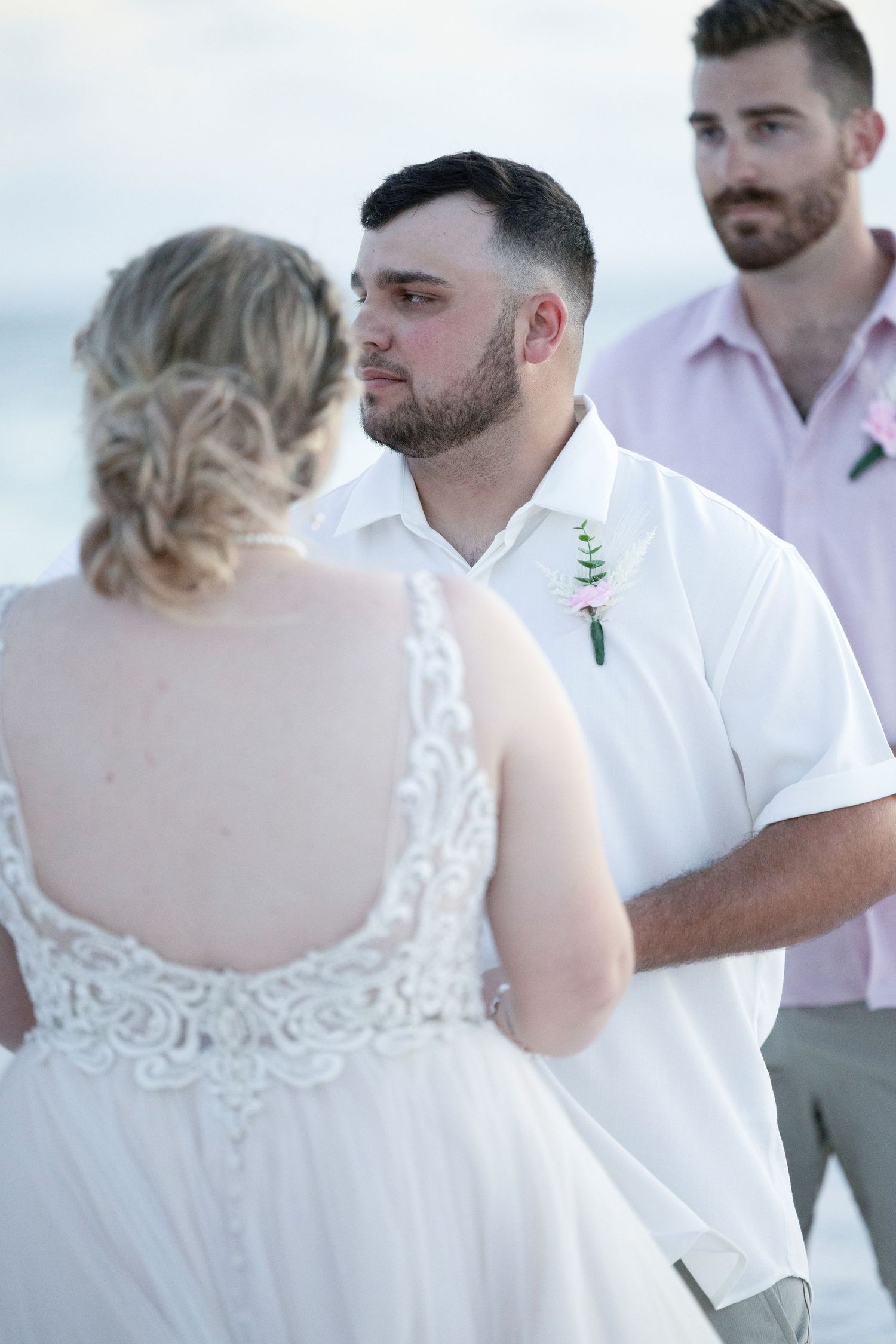 A wedding party stands in a row wearing white shirts and formal attire at an outdoor ceremony.