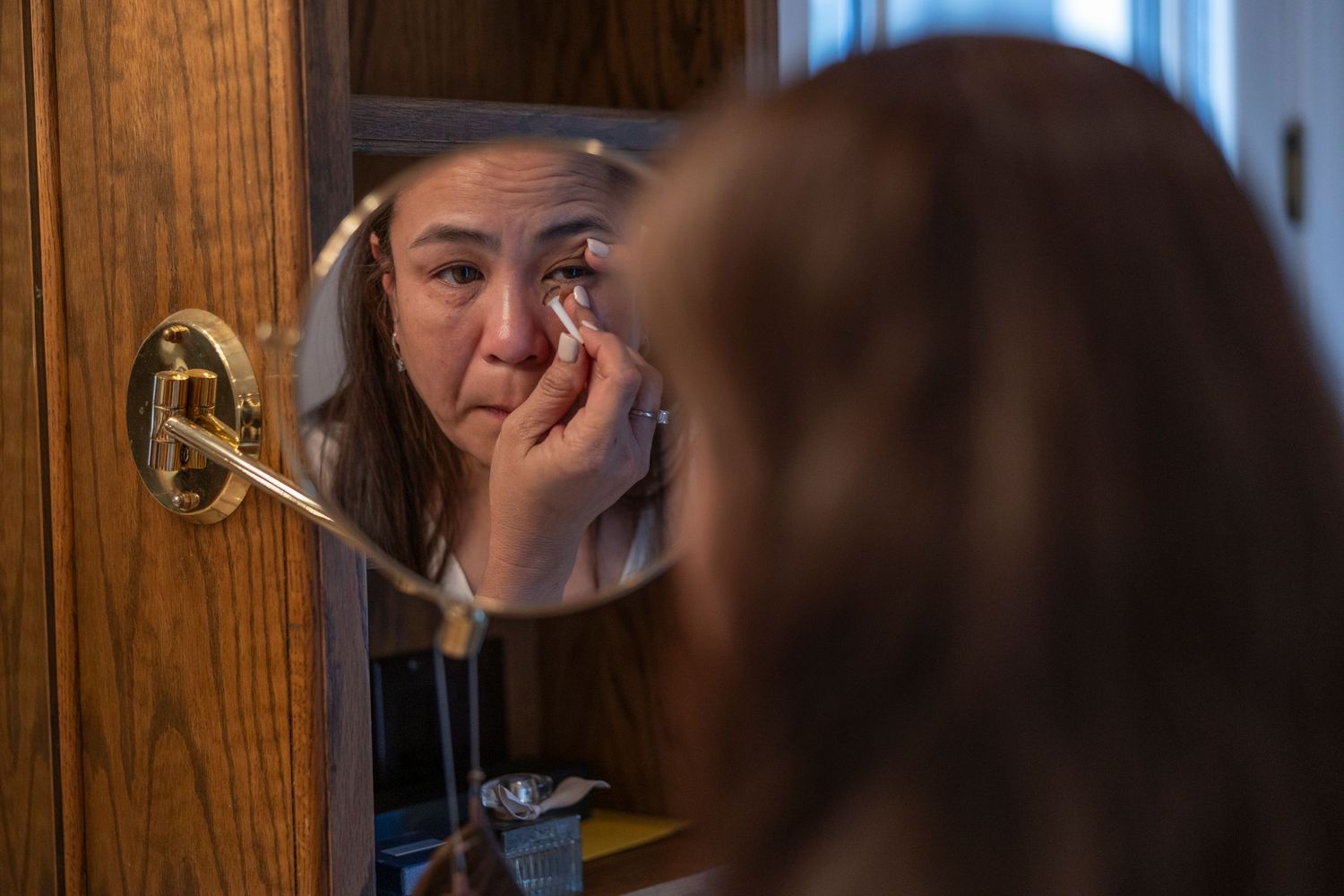 Woman applying eye makeup while looking in a wooden framed bathroom mirror.