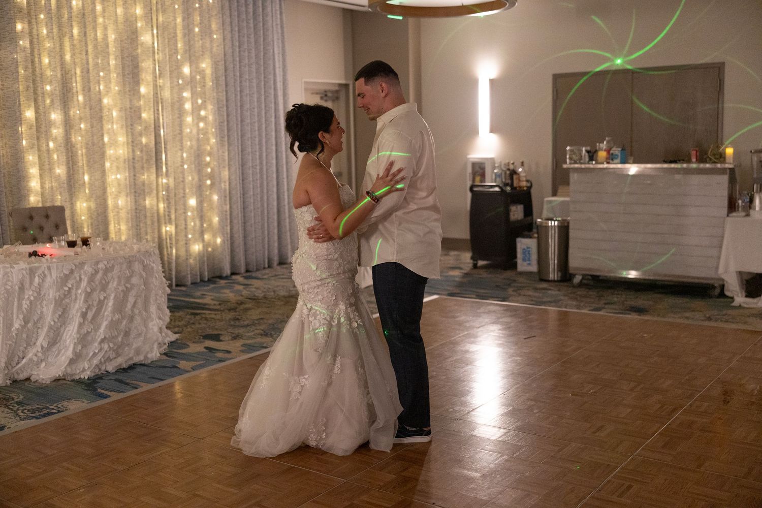 Bride and groom share their first dance on a wooden dance floor, surrounded by fairy lights at their wedding reception.