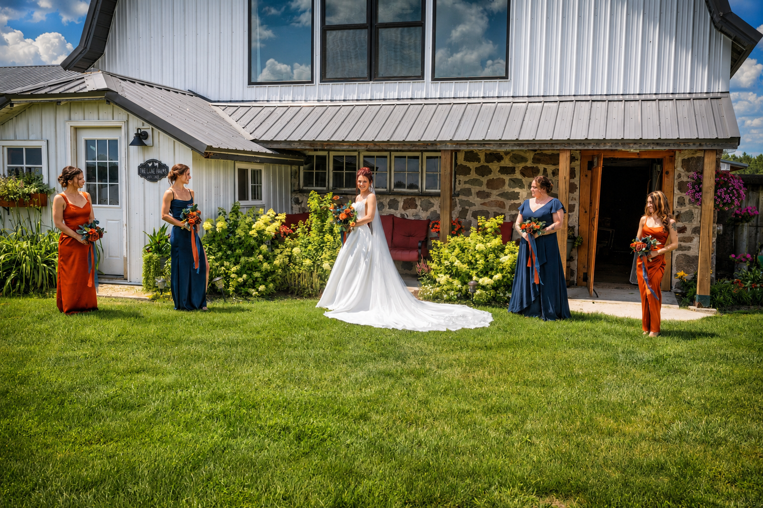 Bride in white gown poses with bridesmaids in navy blue dresses outside a rustic barn venue on a sunny day.