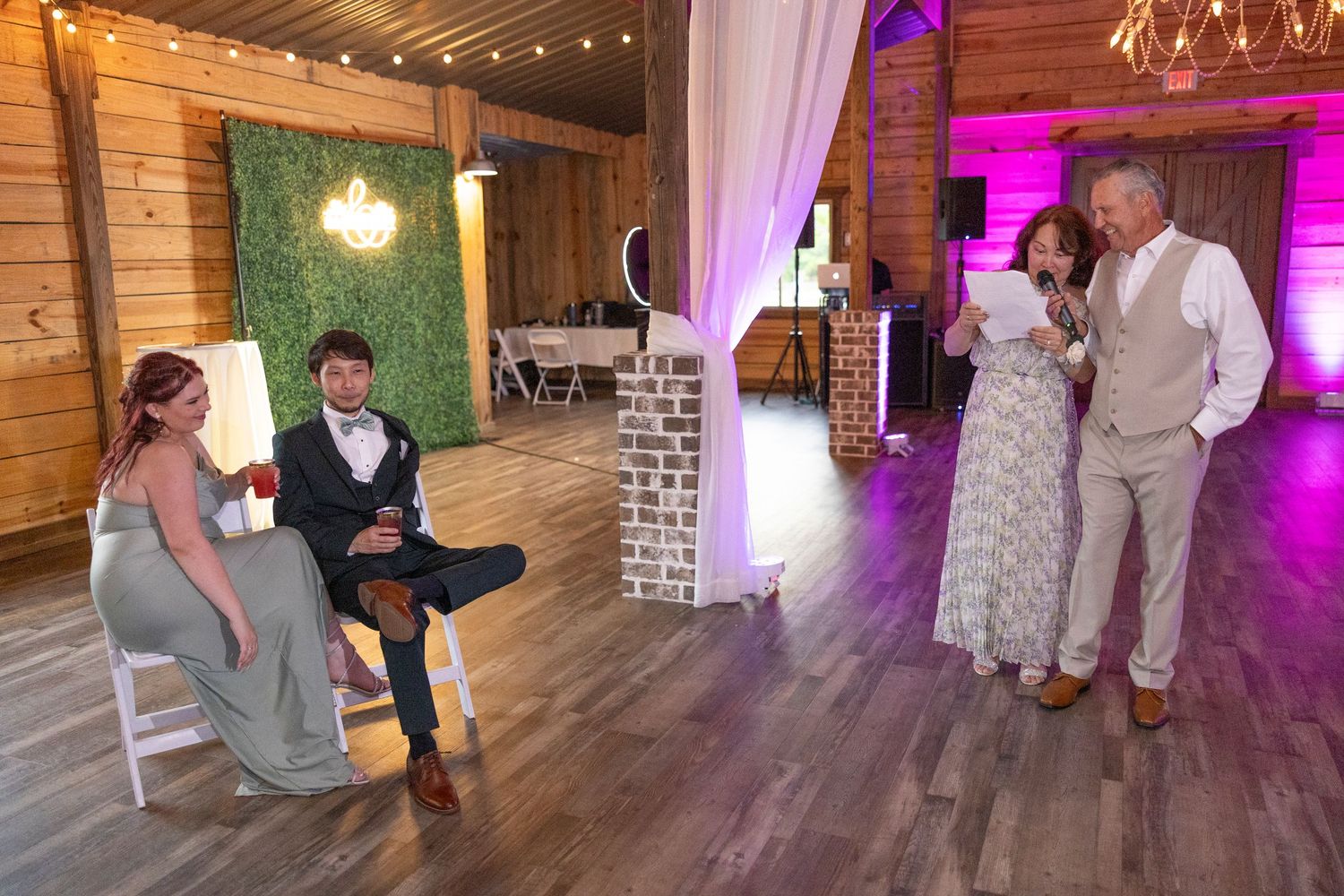 People dancing and celebrating at a rustic barn wedding reception with string lights and purple uplighting.