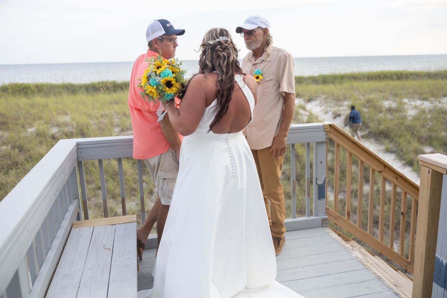 Wedding ceremony takes place on a wooden deck overlooking a scenic beach and ocean view.