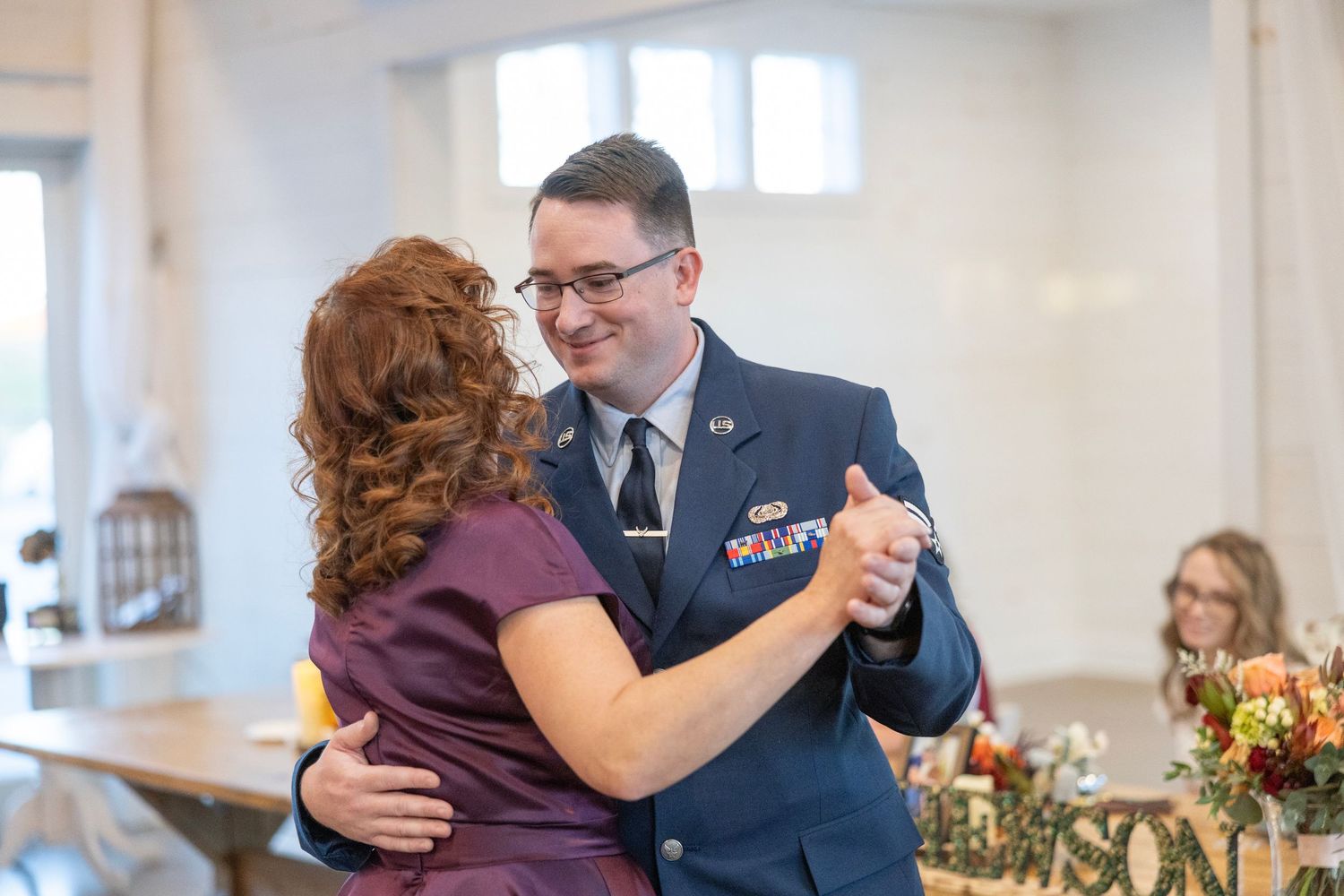A couple dances together at an indoor venue with decorative floral arrangements visible in the background.