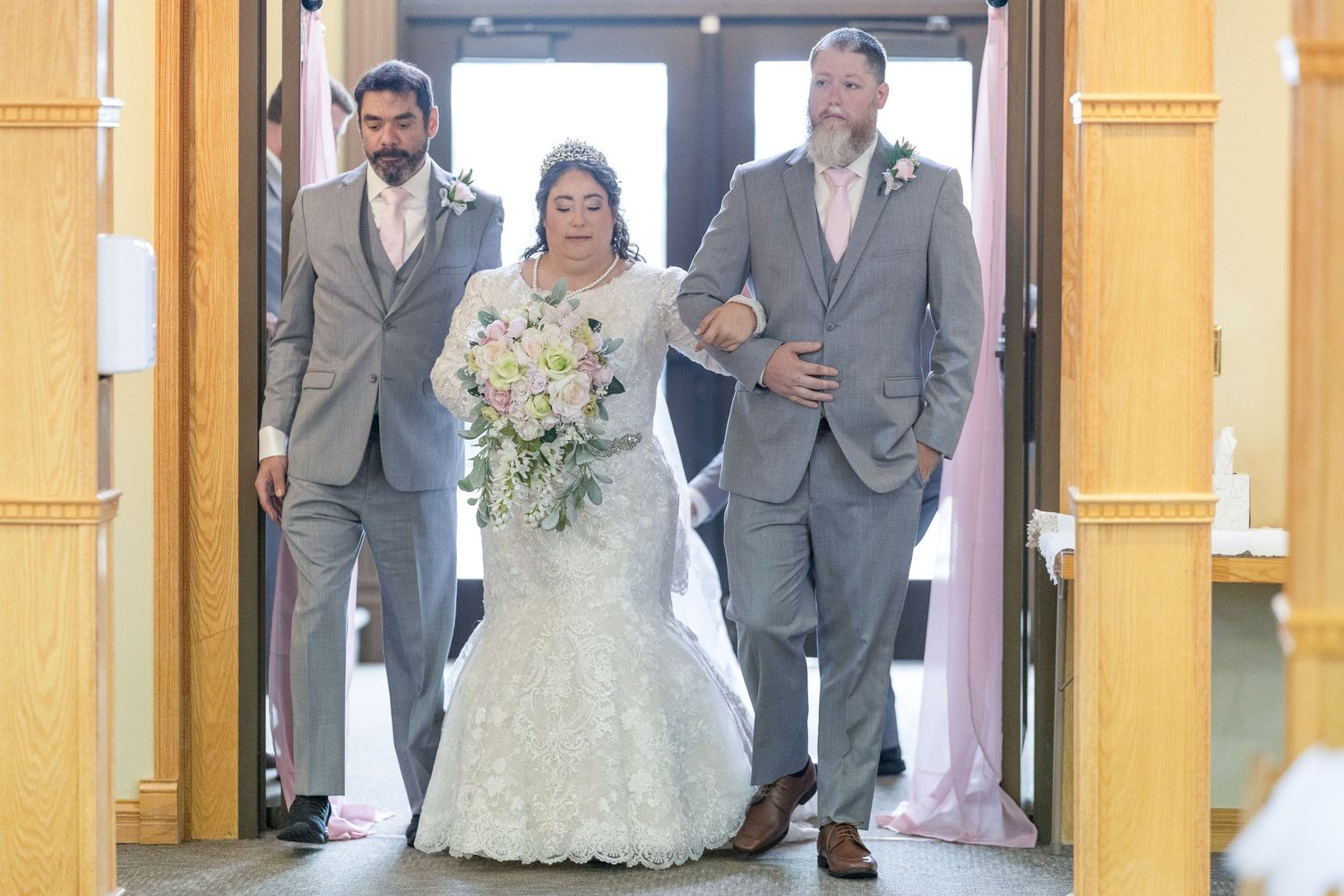 A wedding party poses in formal attire between elegant yellow columns during an indoor celebration.