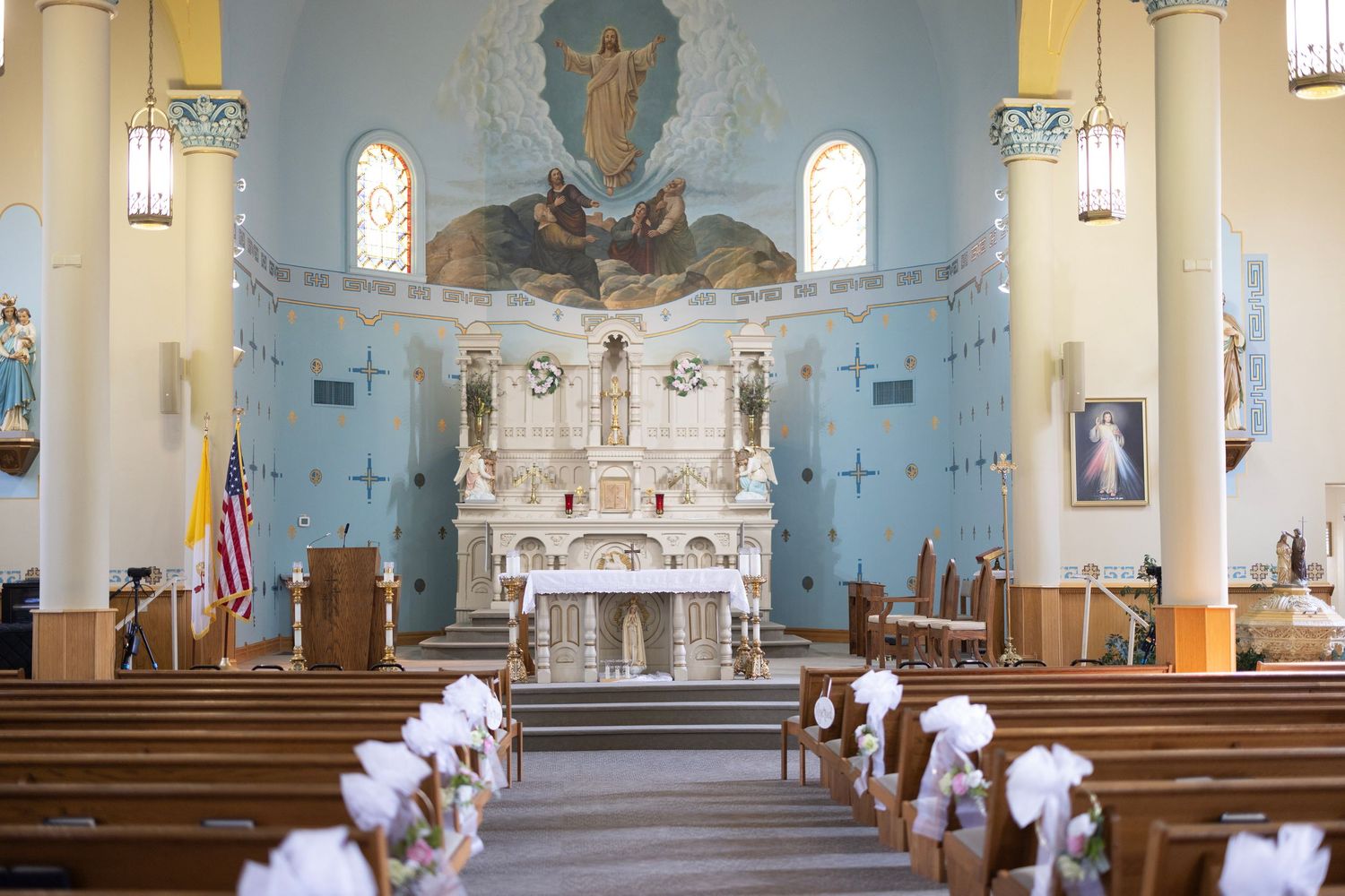 Interior view of a traditional Catholic church sanctuary with white walls, stained glass windows, and ornate altar decorations.