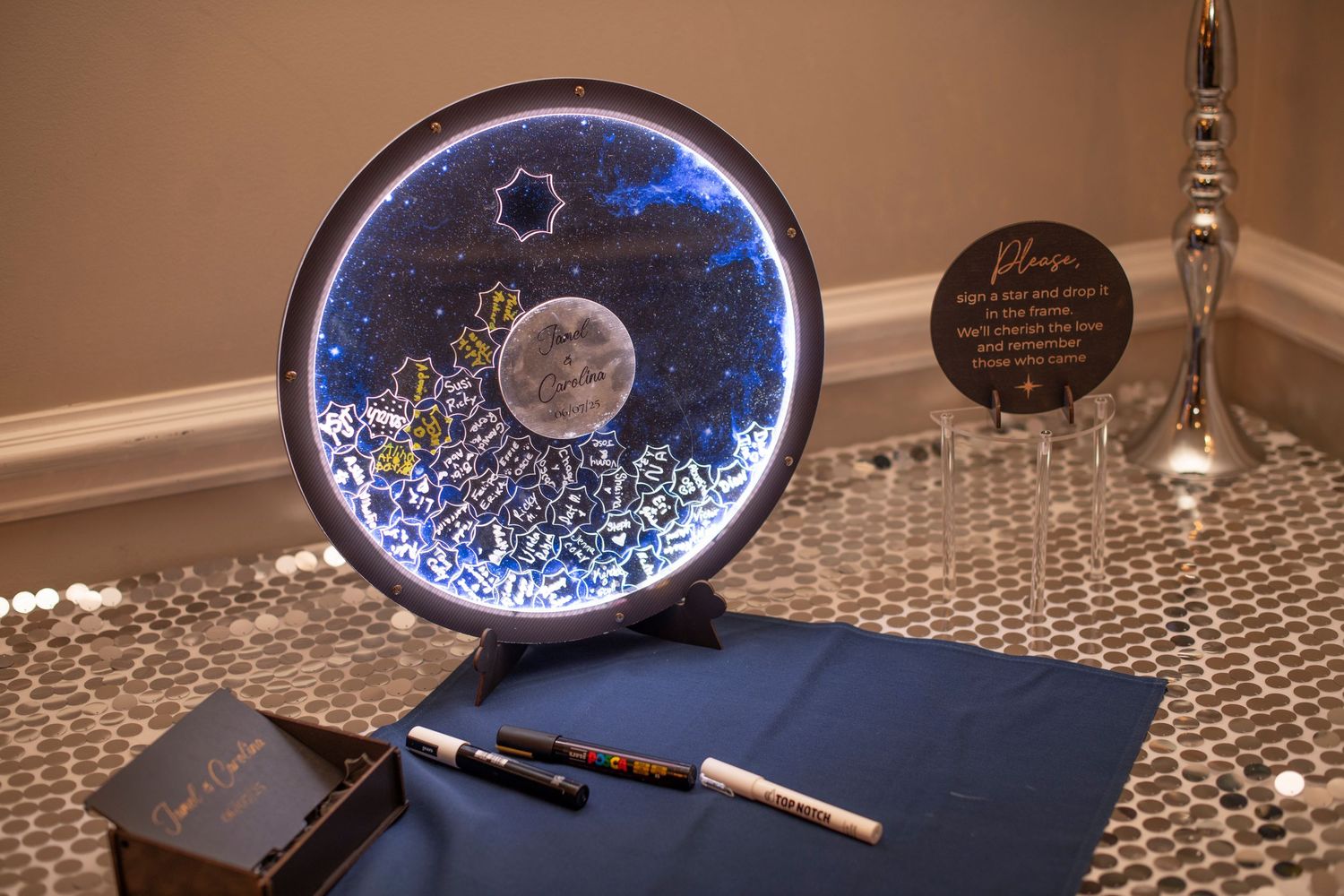 A circular LED moon lamp glows with blue light next to a notebook and pen on a textured surface.