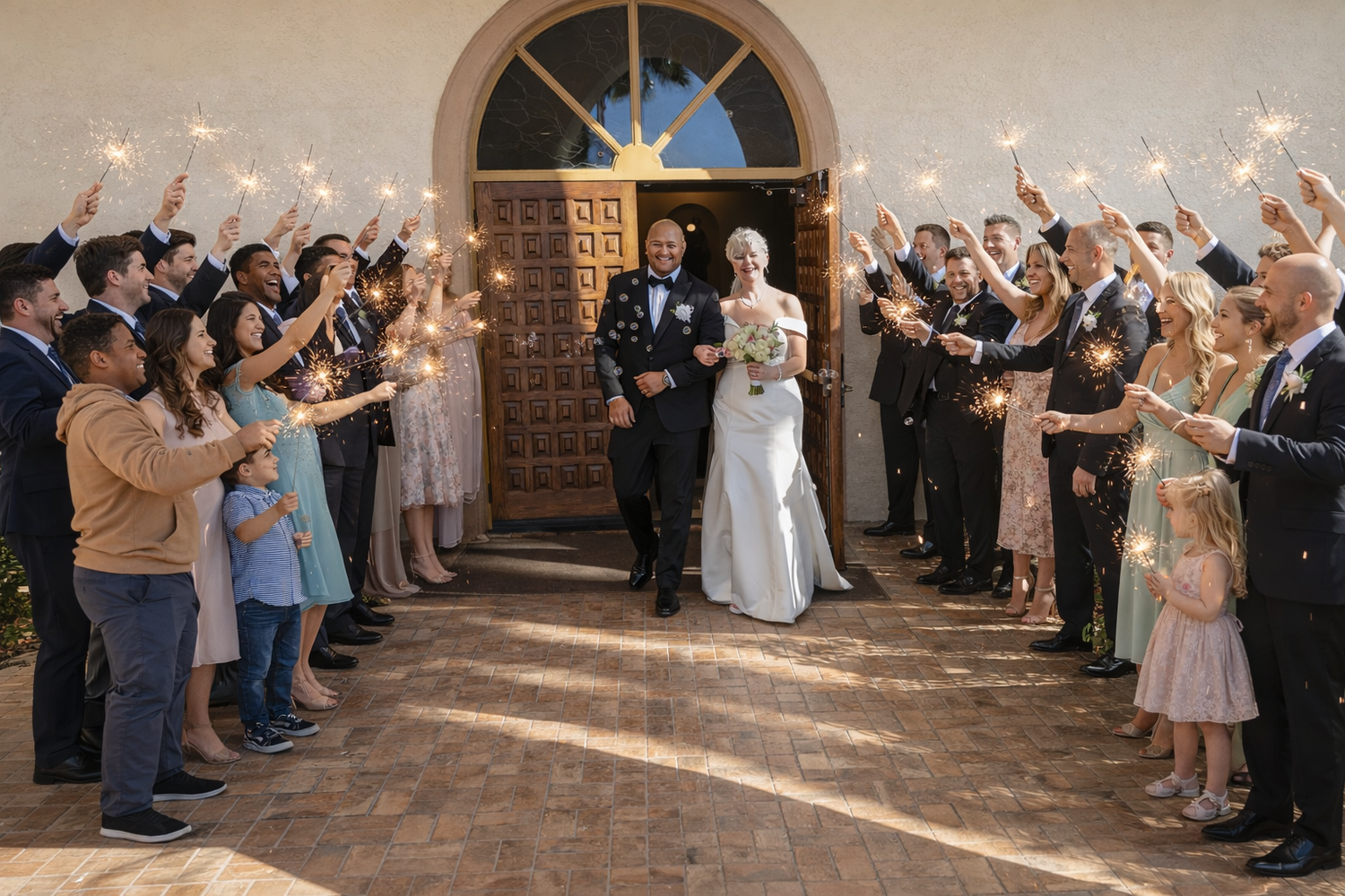Wedding guests line a covered walkway holding sparklers to celebrate as newlyweds exit their reception ceremony.