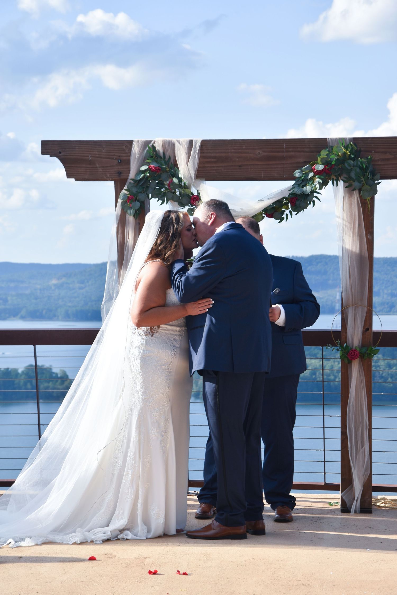 A romantic lakeside wedding ceremony sequence shows a couple sharing their first kiss under a wooden pergola.