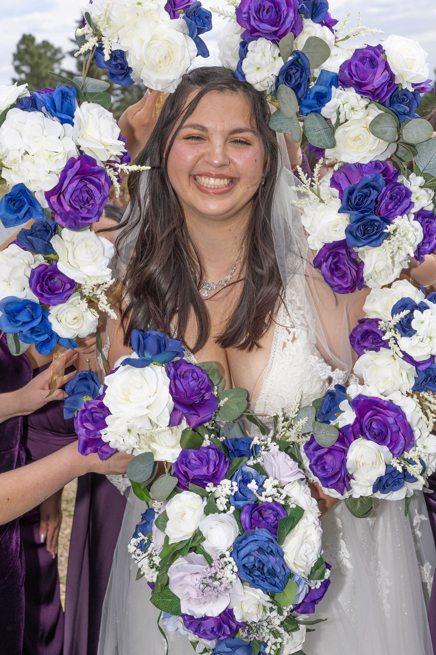 Wedding bouquet arrangement featuring purple, blue and white roses with silver accents against a light background.