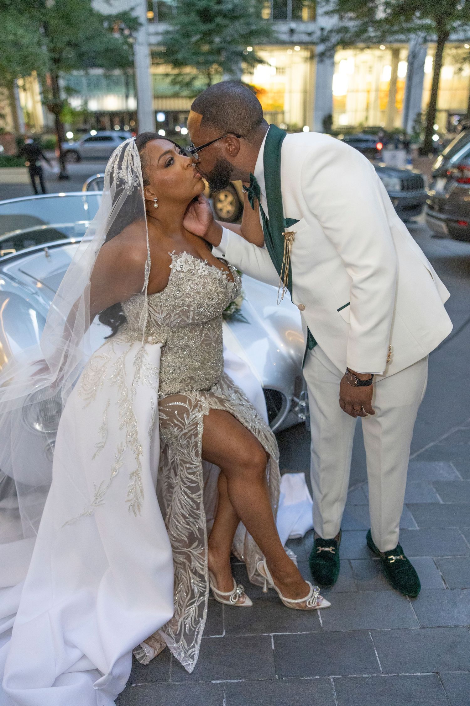 A couple shares a romantic kiss on their wedding day in formal white attire and a flowing veil.