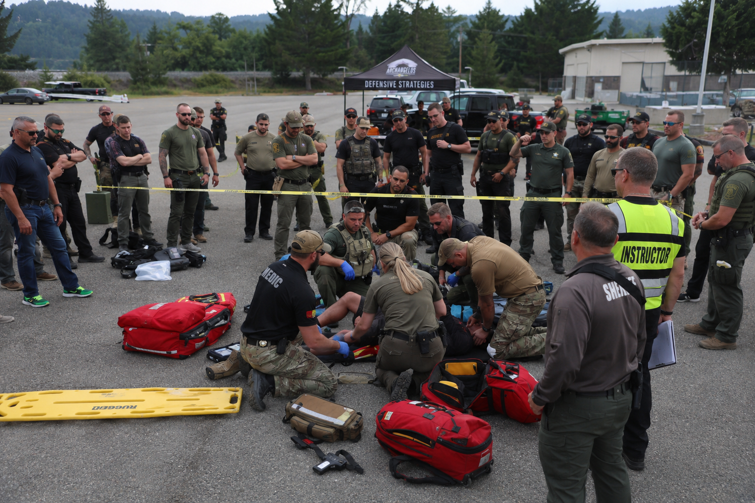 Emergency responders in tactical gear conduct a medical training exercise outdoors behind yellow police tape.