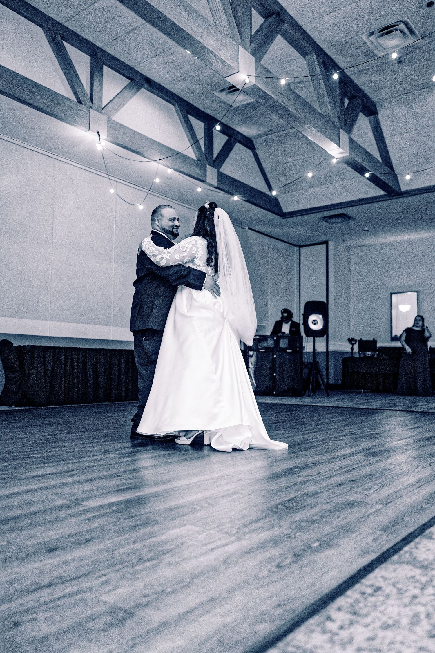 Bride and groom share their first dance in a elegant ballroom with string lights and wooden ceiling beams.