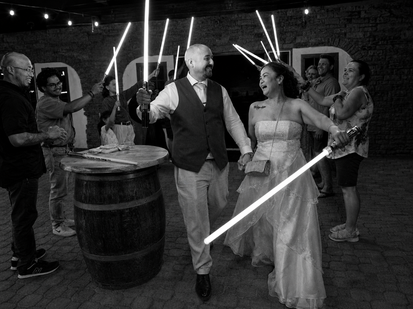 Couple in wedding attire wielding glowing lightsabers at Star Wars themed wedding reception in black and white photo.
