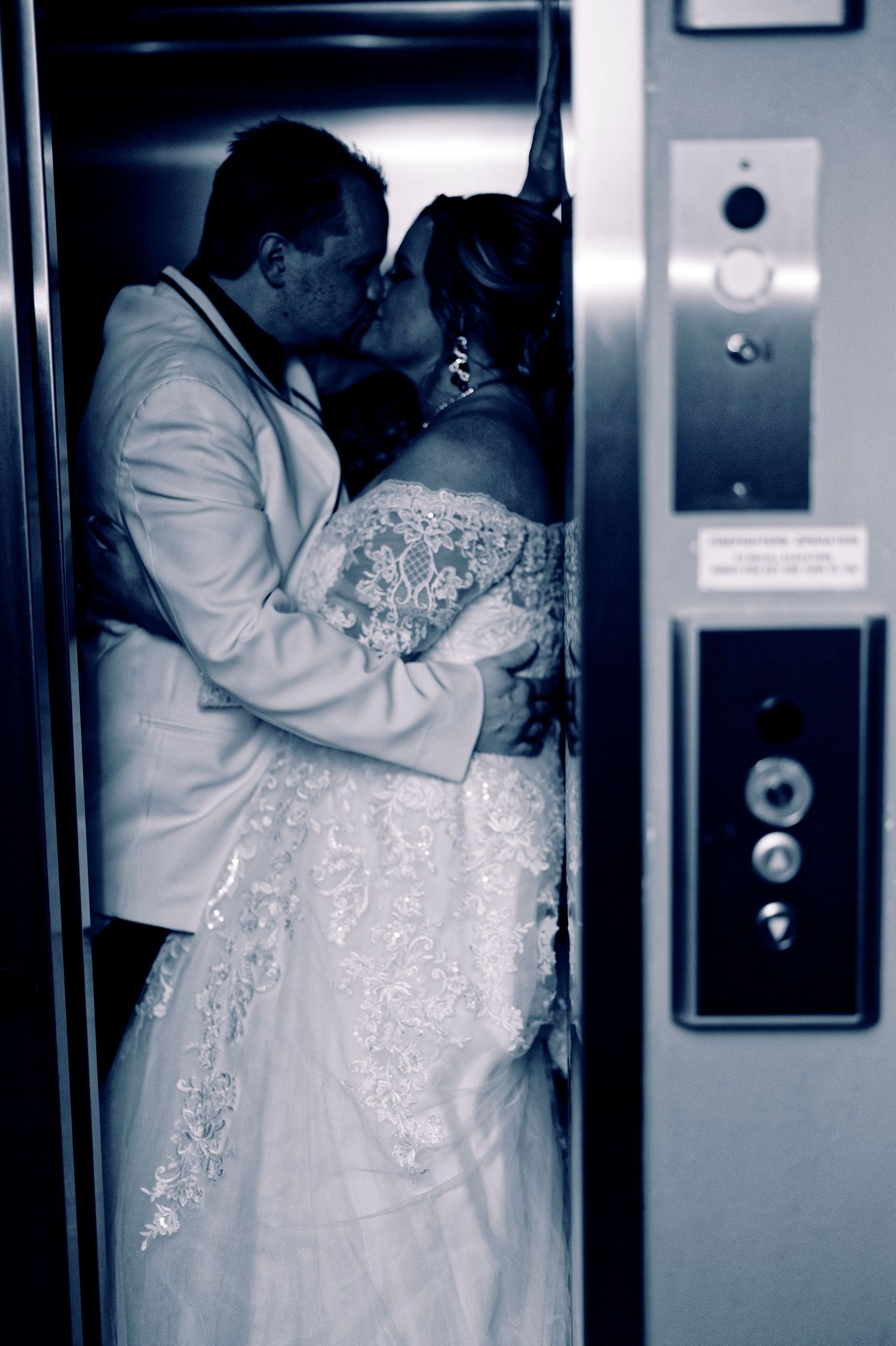 Bride and groom sharing a romantic kiss in an elevator, captured in a stunning blue-toned black and white wedding photo.