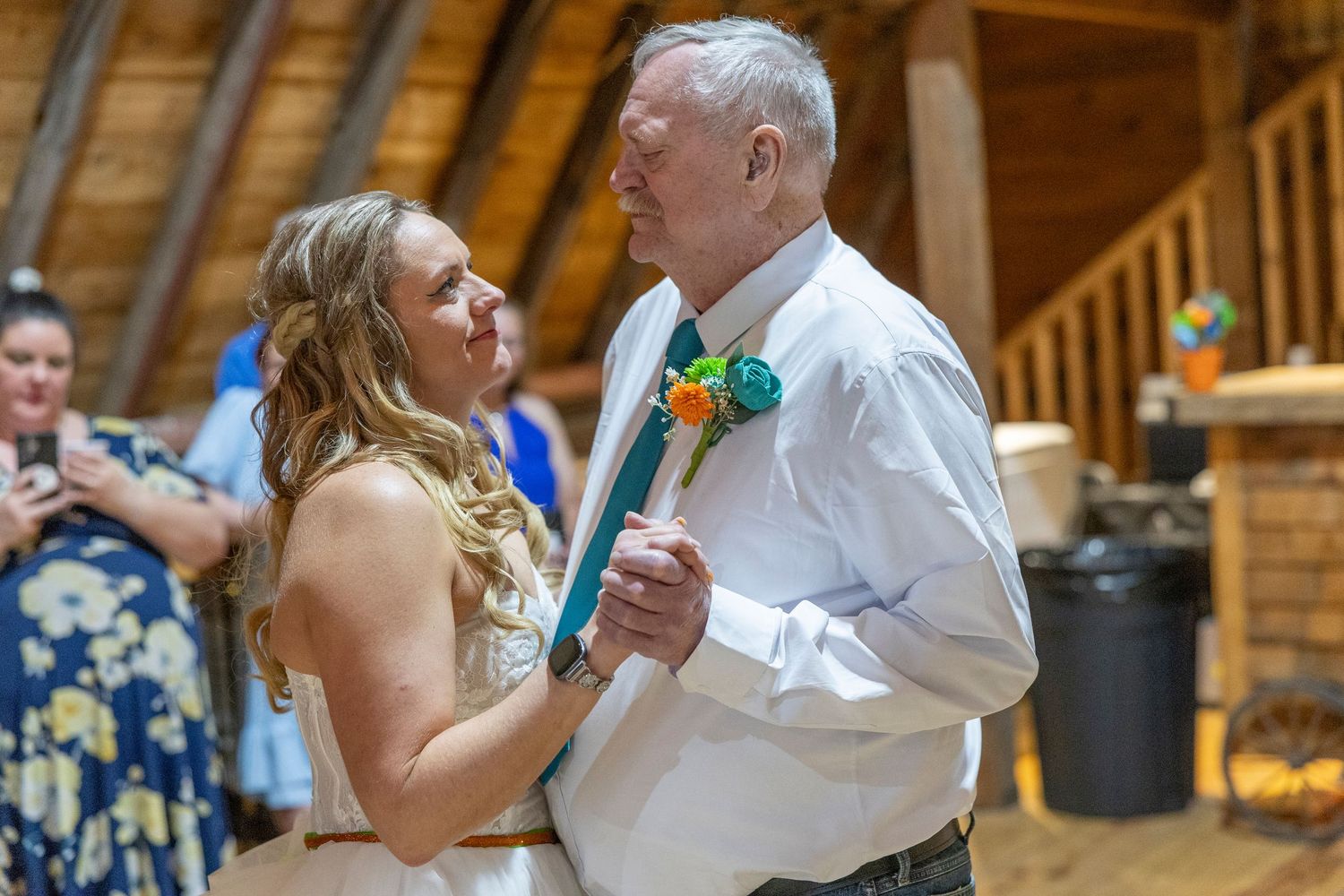 Bride and older man share a father-daughter dance in a rustic wooden barn at a wedding reception.