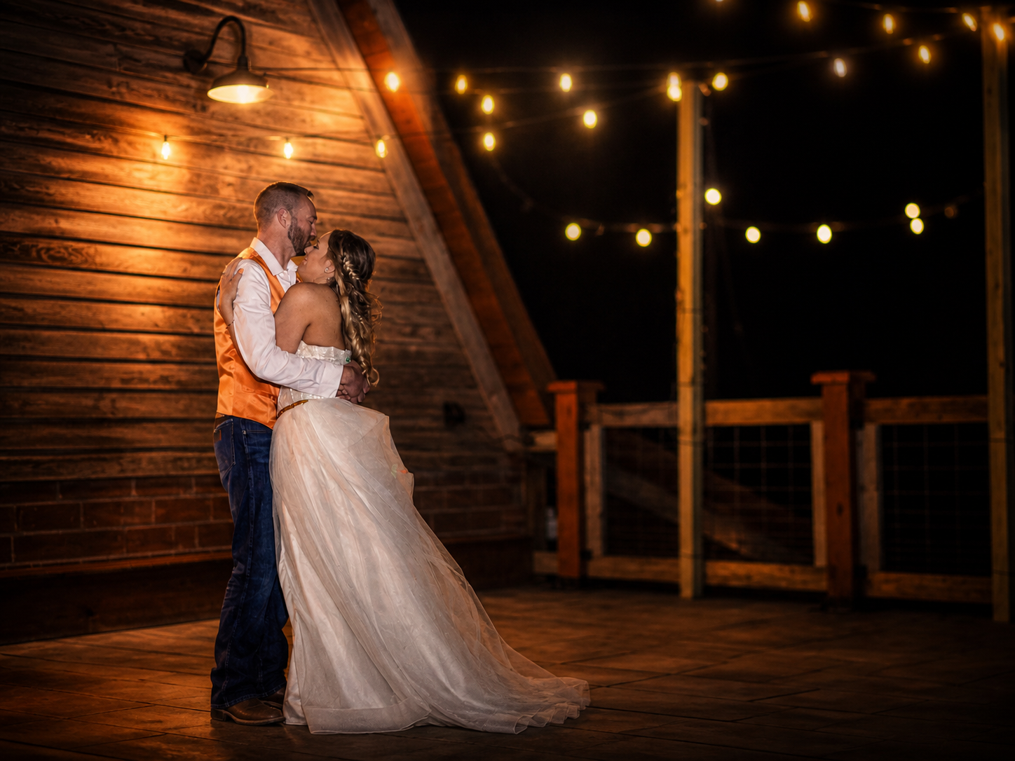 Couple shares romantic first dance in rustic barn wedding venue with warm string lights glowing at night.