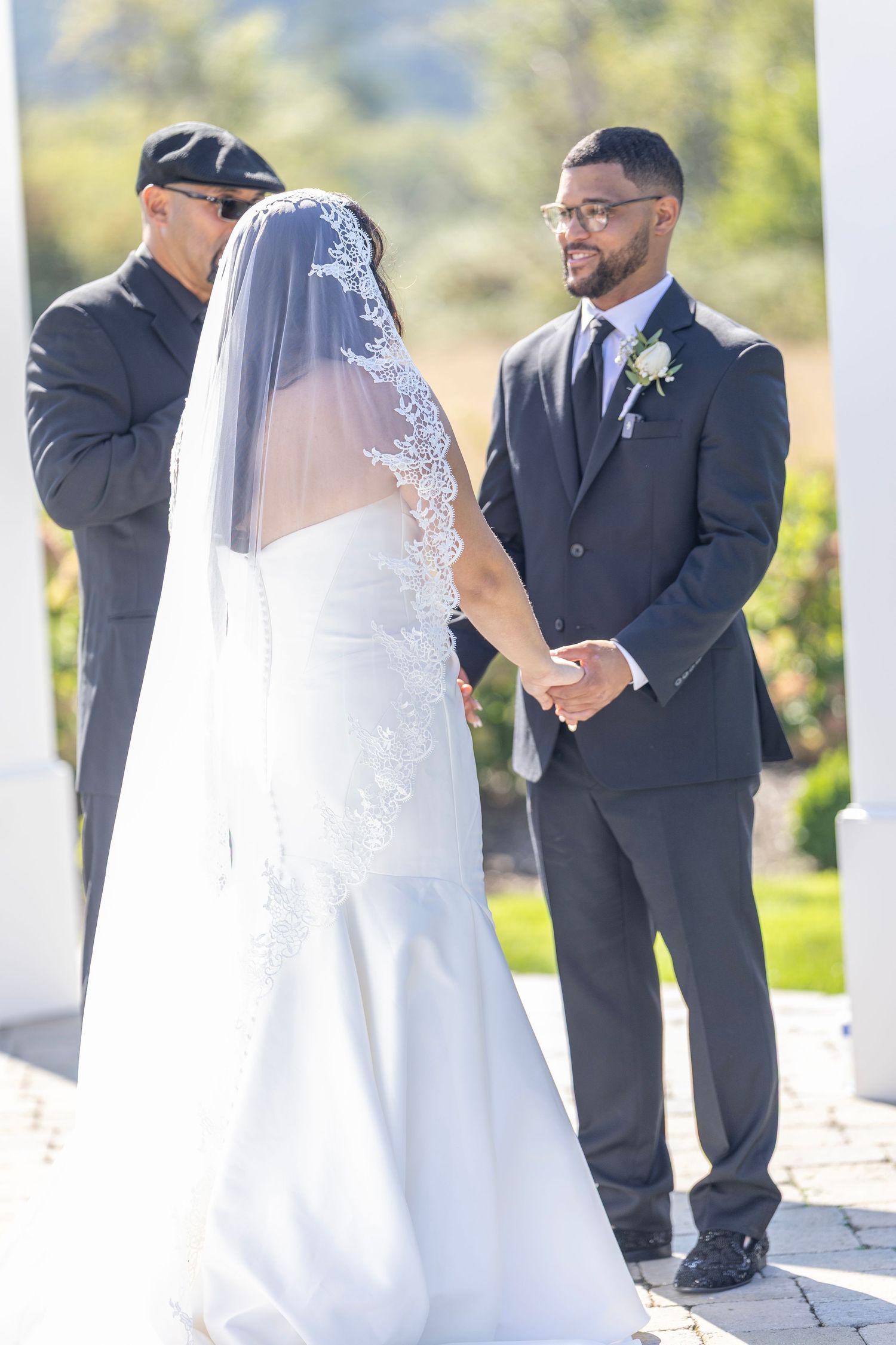 Wedding ceremony takes place outdoors with participants in formal black suits and white wedding gown.
