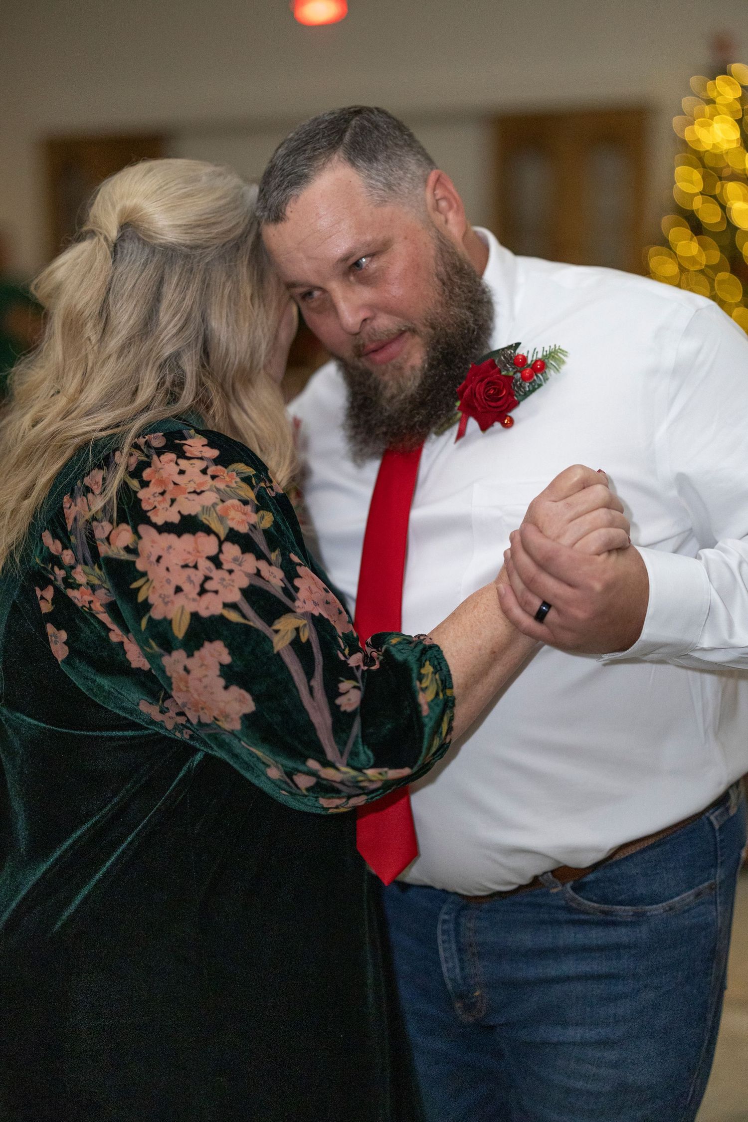 A couple in formal attire performs a dip dance move in front of holiday lights and decorations.