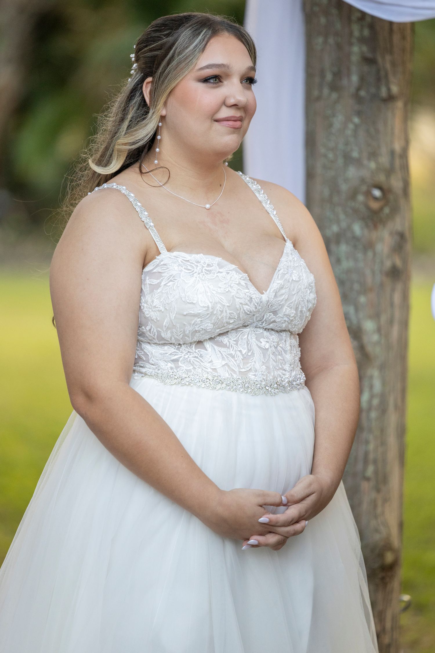 Beautiful wedding portrait featuring a bride in a white lace and tulle gown with spaghetti straps standing outdoors.