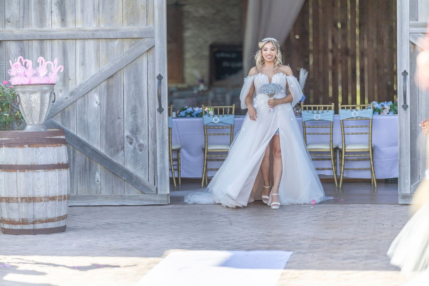 A bride in a white wedding gown sits gracefully on rustic wooden stairs at a barn venue.