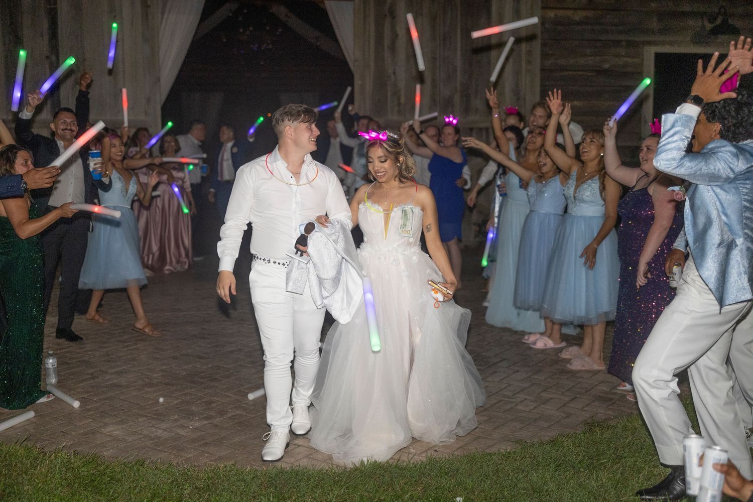 Wedding guests create a glowing exit path with LED light sticks as newlyweds walk through in celebration.
