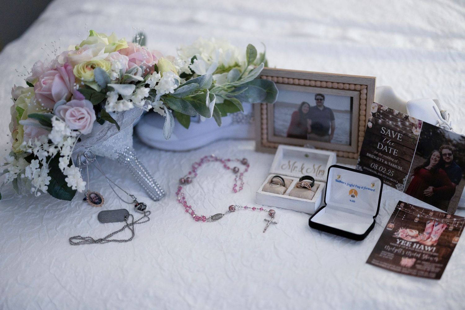 Elegant wedding details including rings, flowers, and photographs arranged on a light colored surface.