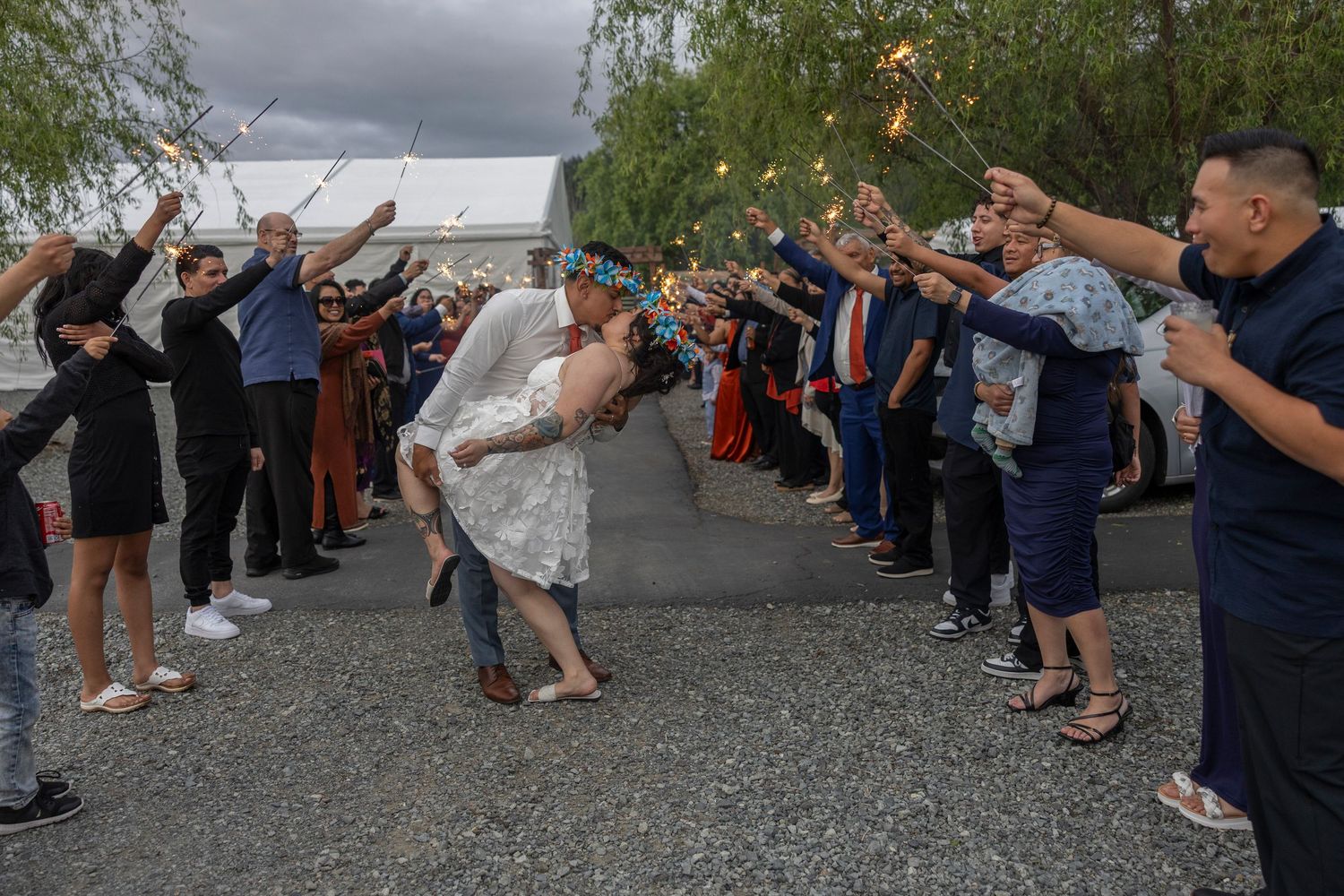Wedding guests form a cheerful tunnel with raised arms for the newlyweds to walk through during an outdoor celebration.
