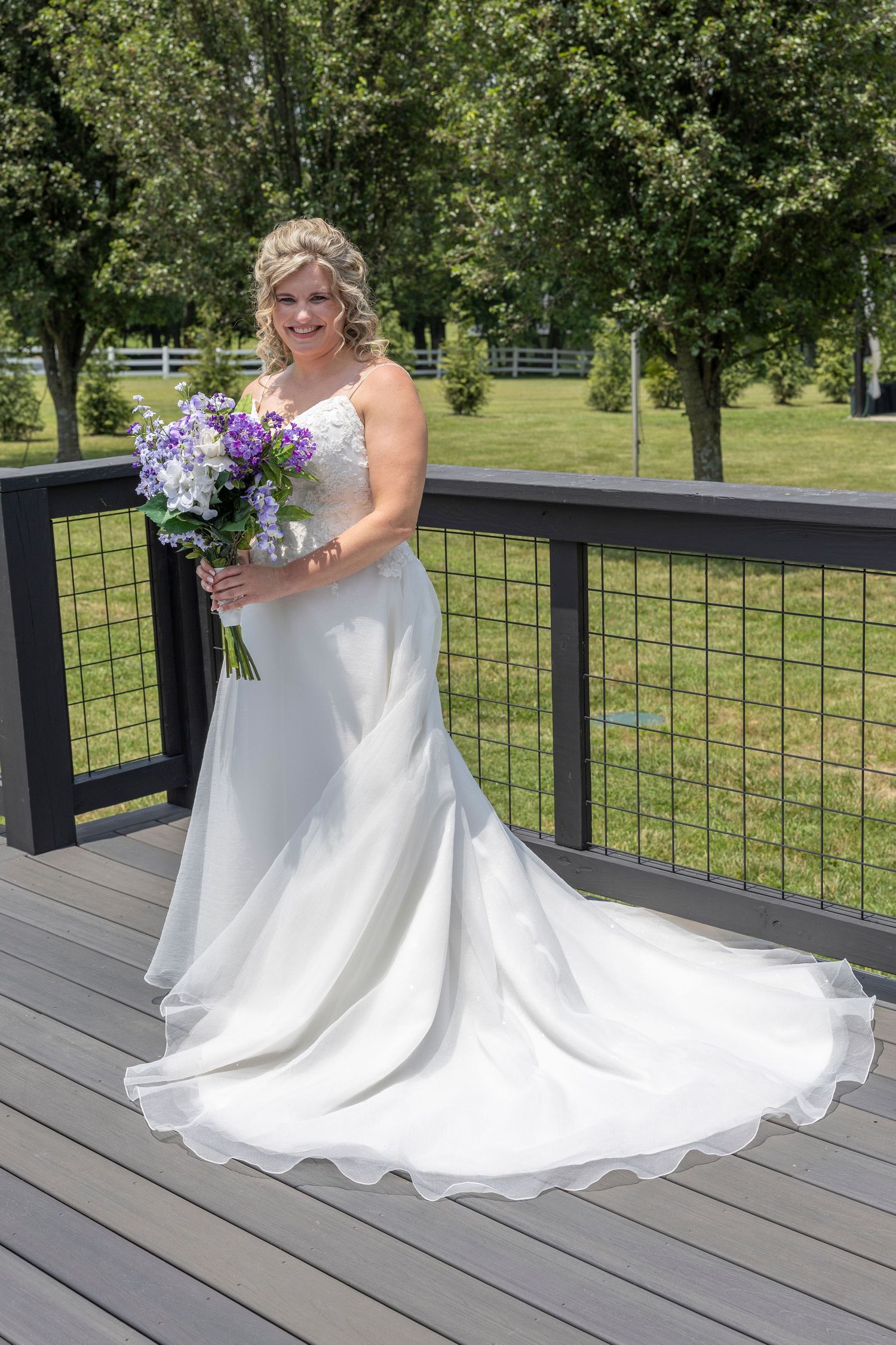 A bride in a flowing white wedding dress twirls gracefully on a wooden deck surrounded by lush greenery.
