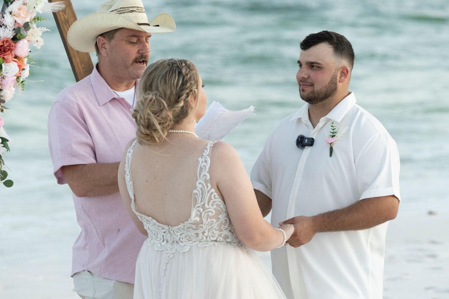 A couple shares a tender moment during their beach wedding ceremony with guests looking on in the background.