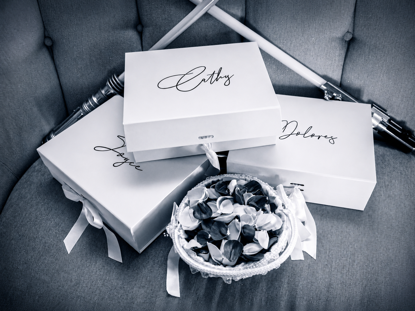 Black and white photo of personalized white gift boxes labeled Cathy, Joyce, and Dolores with a small floral arrangement.
