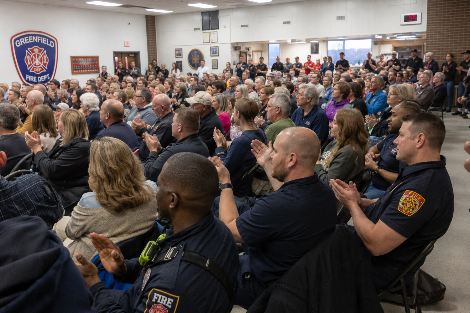 Firefighters and community members applaud at a packed Greenfield Fire Department meeting inside the fire station.