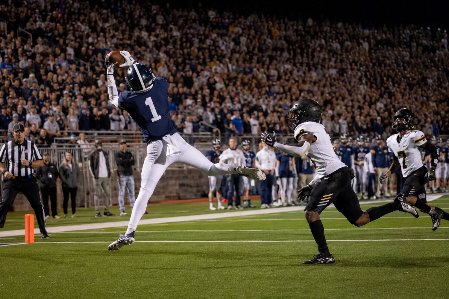 Wide receiver in blue uniform catches touchdown pass in the end zone during night game.