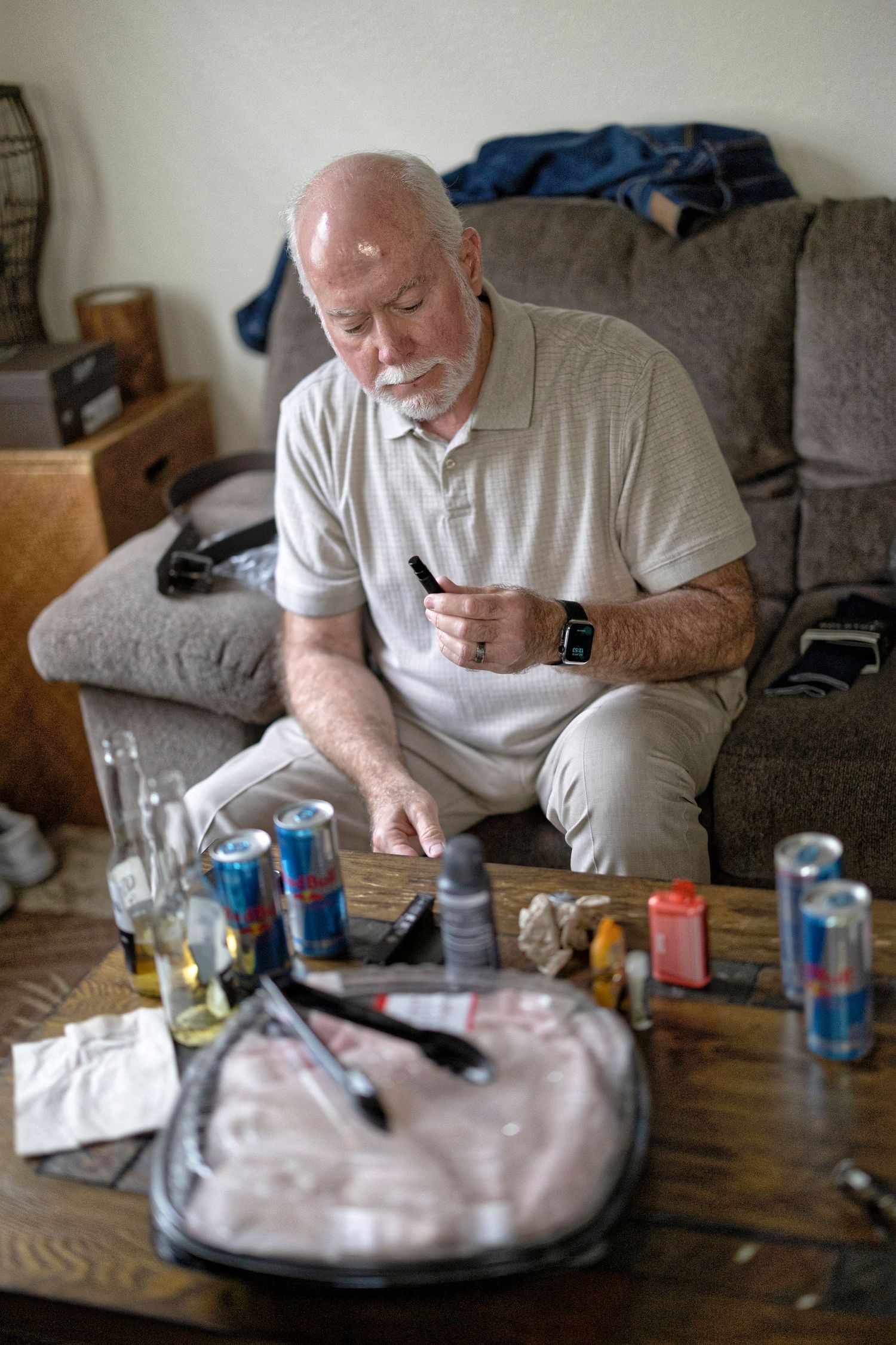 Person in white polo shirt sitting on couch with various items and beverages scattered on coffee table.