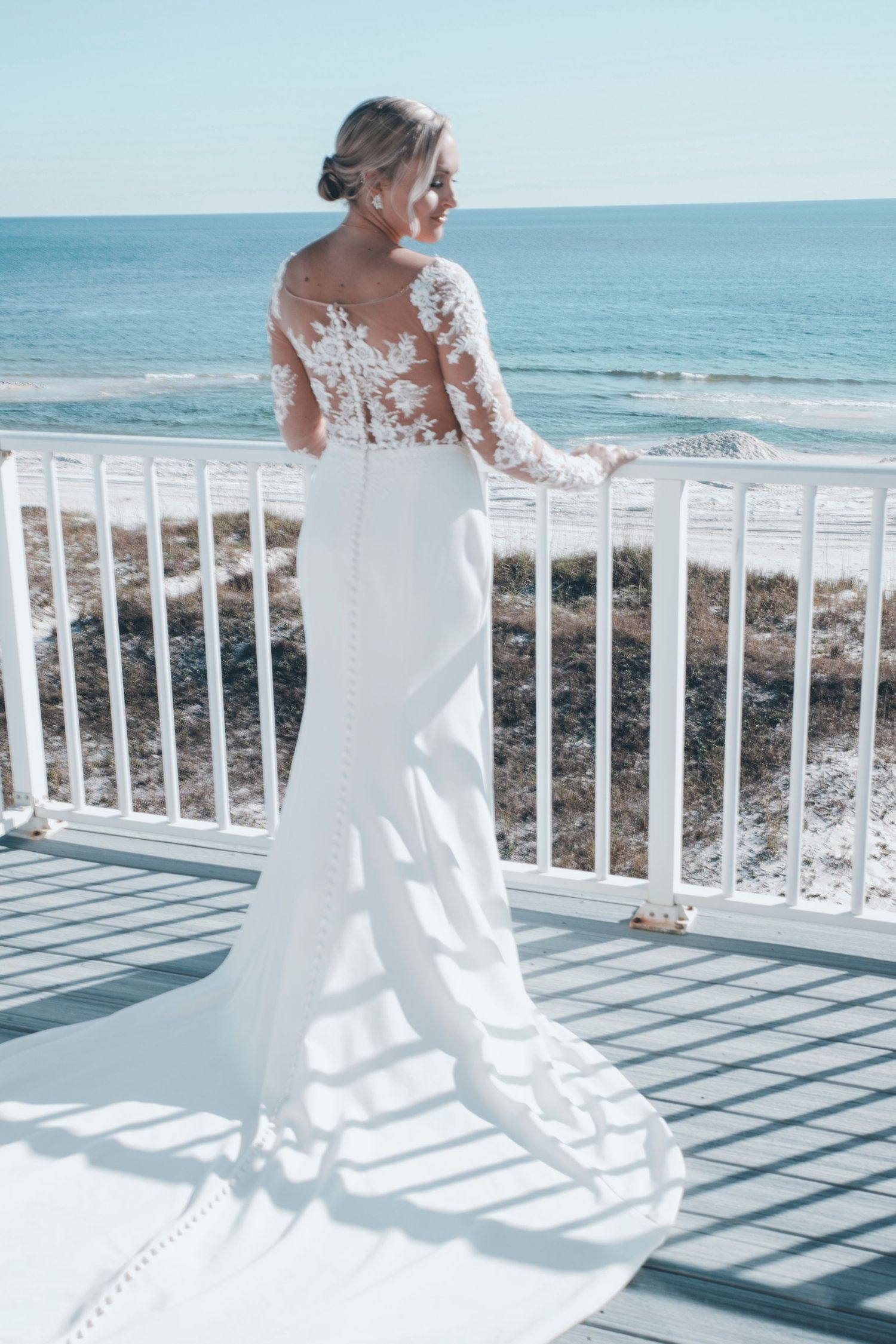 A flowing white wedding dress with lace details billows in the ocean breeze on a beachfront balcony.