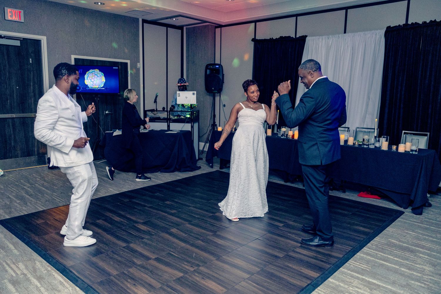 Wedding guests dance together on a dark dance floor at an evening reception celebration.
