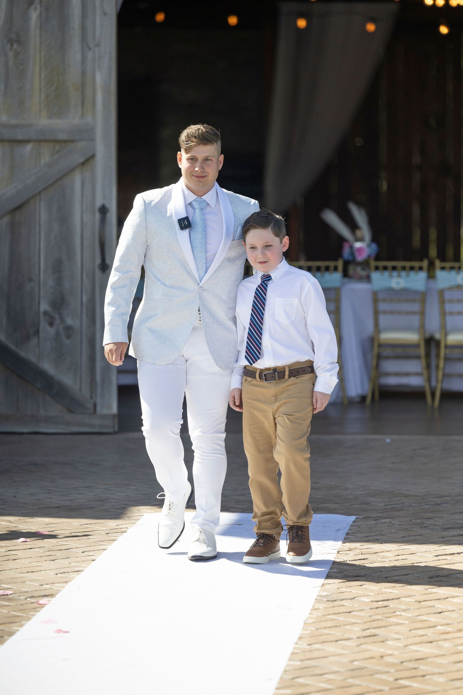 Two people walking together in formal attire, one wearing a white suit and the other in khaki pants and dress shirt.