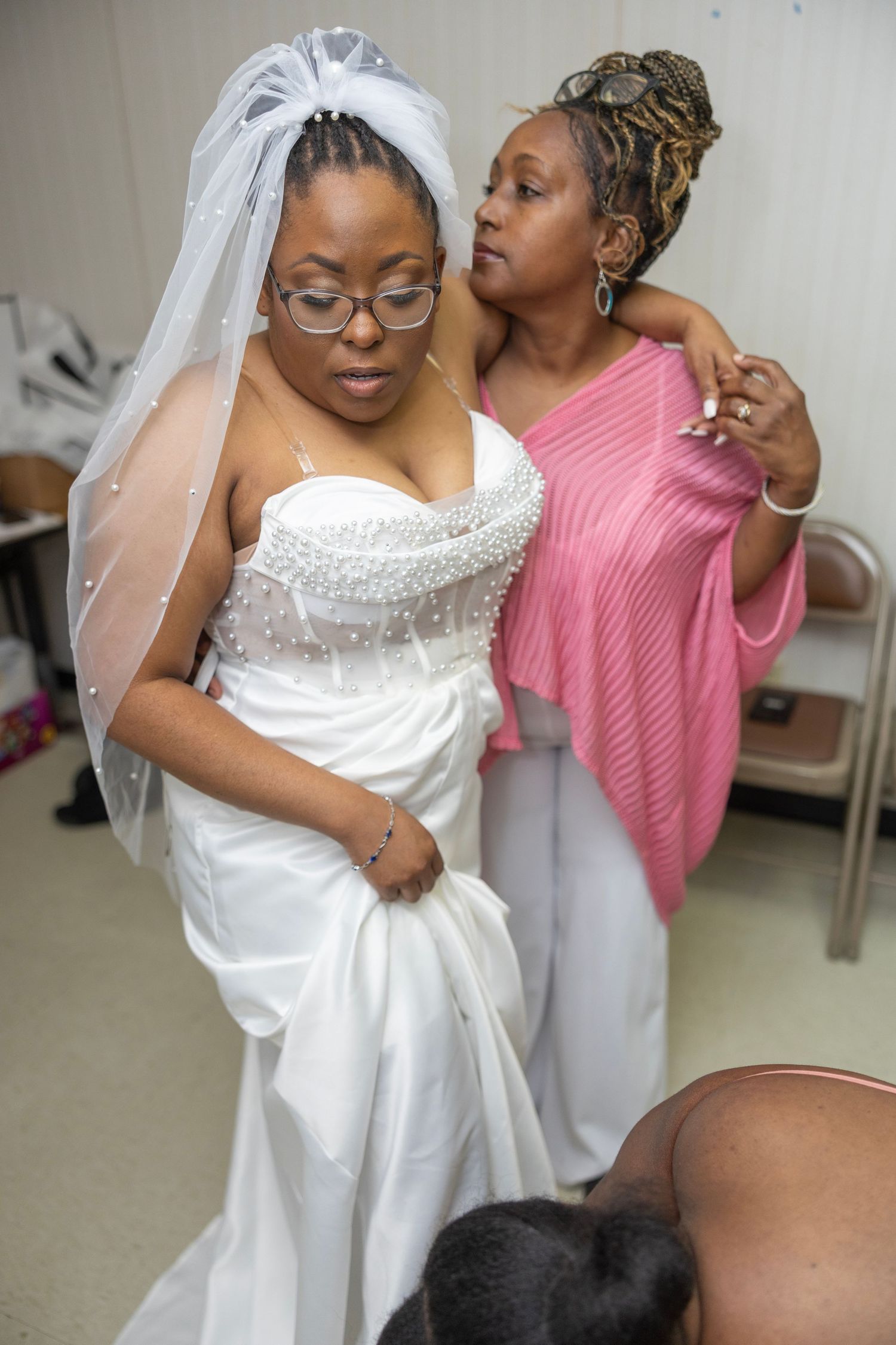 A bride in a white wedding dress and veil gets help with final adjustments to her gown before the ceremony.