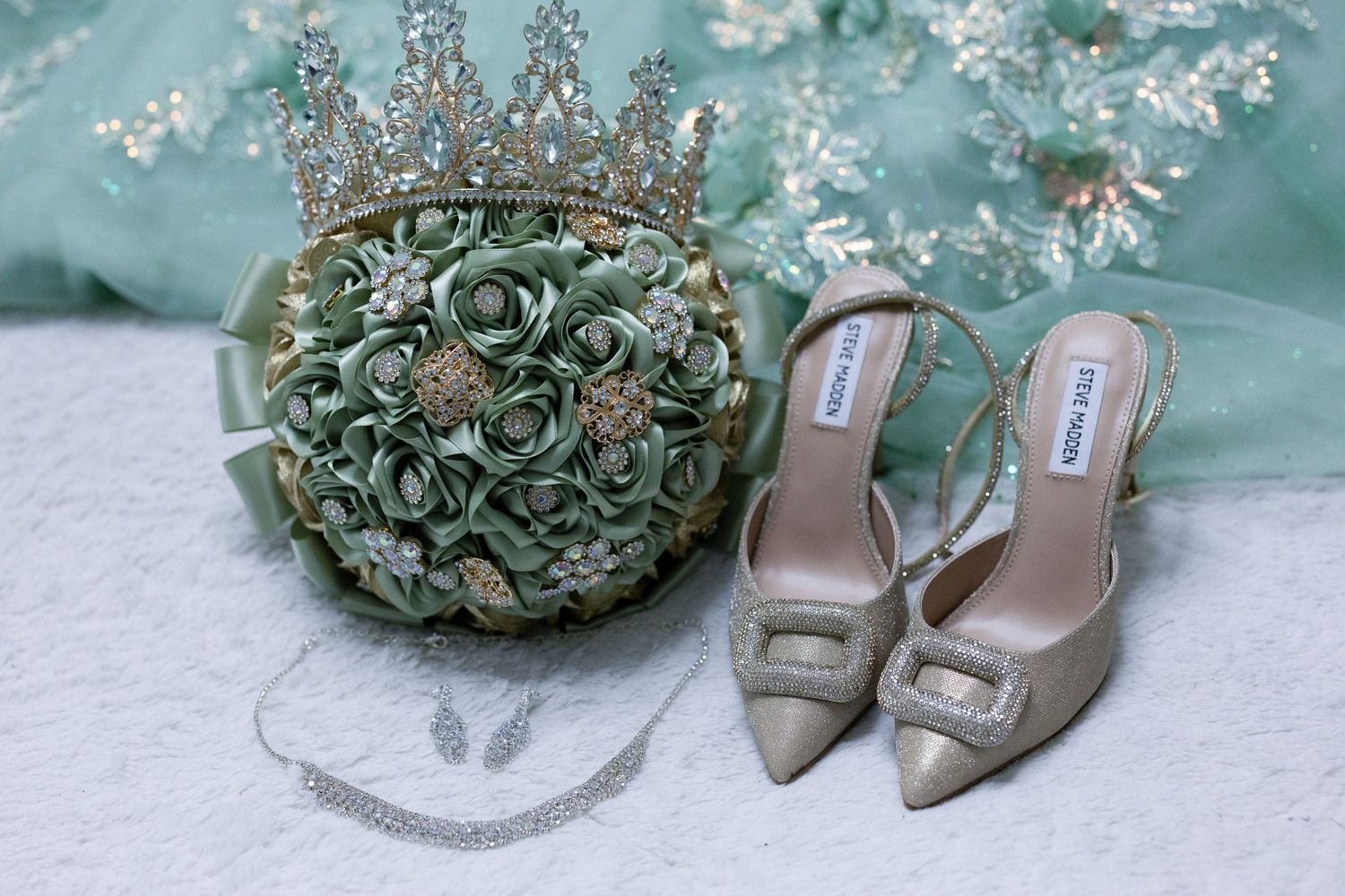 Wedding accessories including a mint green floral bouquet, crystal tiara, and elegant beige slingback heels arranged on lace.