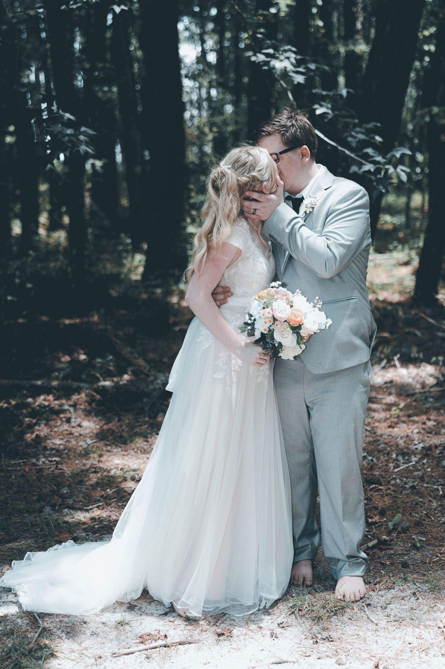 A romantic wedding couple shares intimate moments in a forest setting wearing white and gray attire.