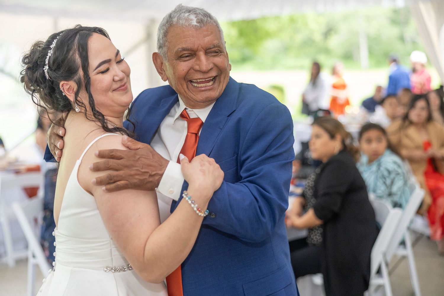 Two people share a joyful dance moment at a wedding reception with guests visible in the background.