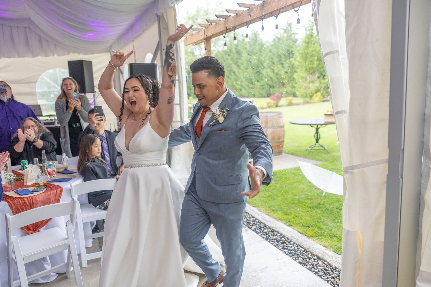Wedding guests dance and celebrate under a white tent during an outdoor reception celebration.