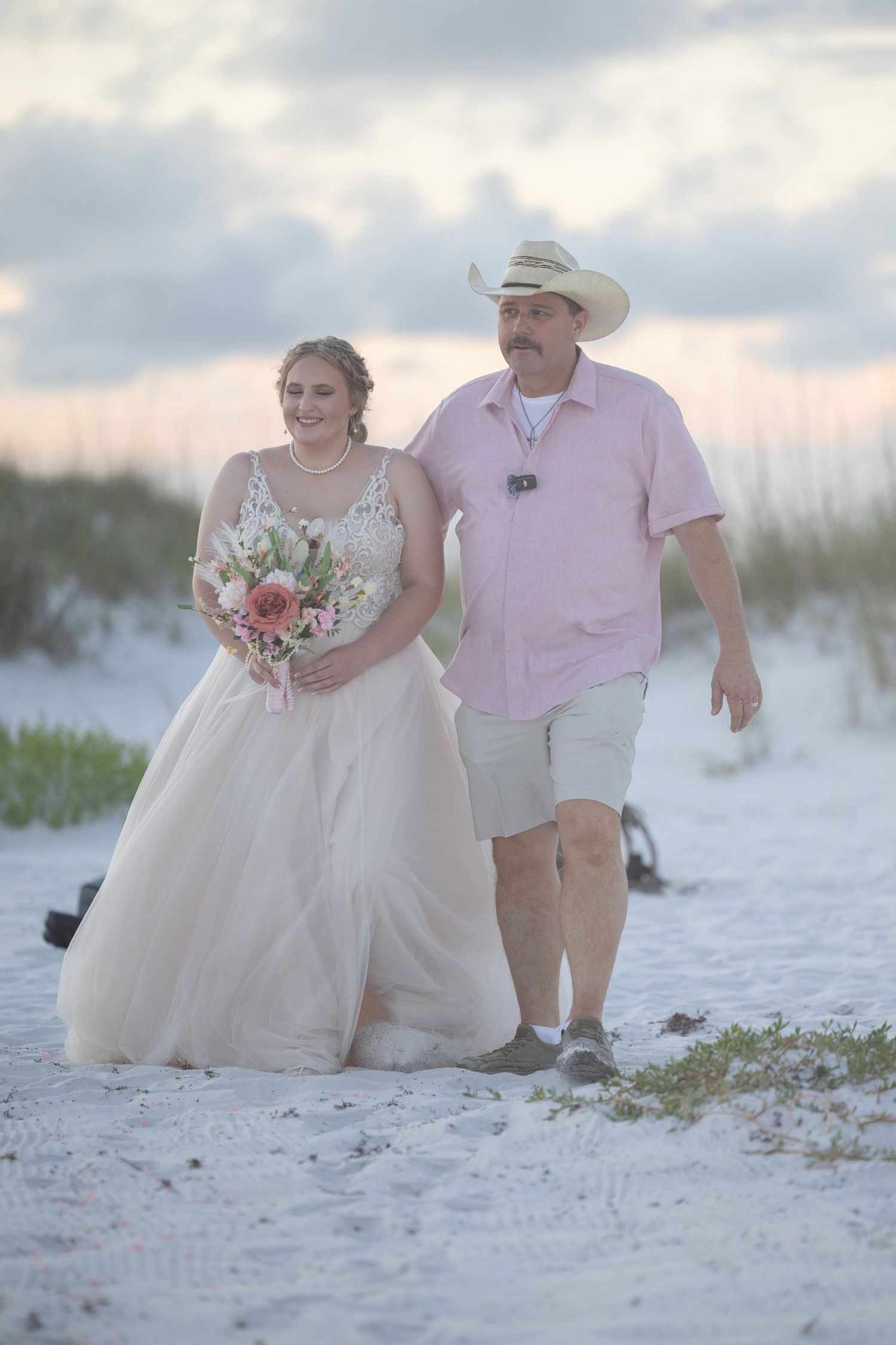 A couple poses together on a white sandy beach at sunset for romantic wedding photos.