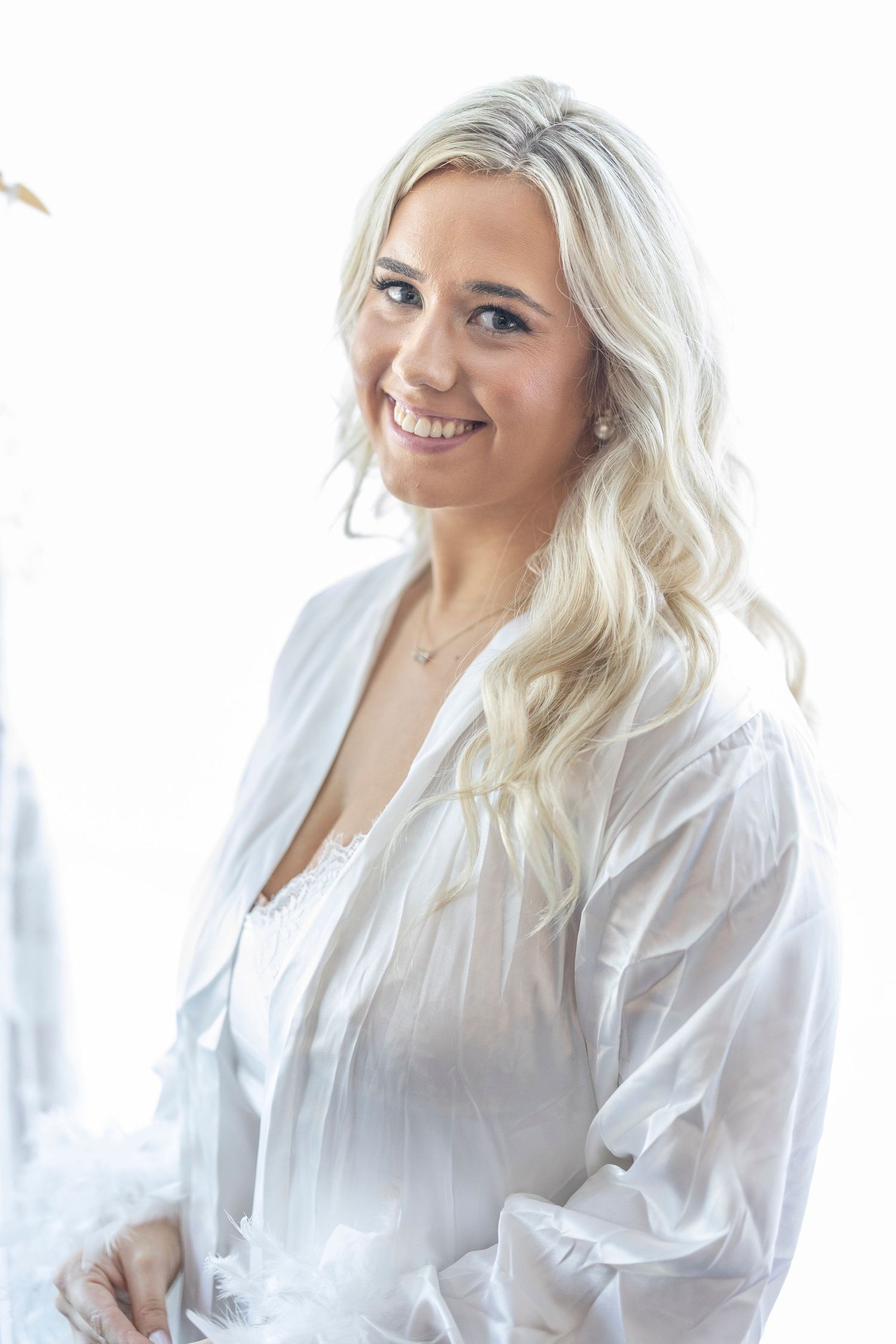 A person with blonde wavy hair wearing a white button-down shirt poses and smiles in a bright indoor setting.