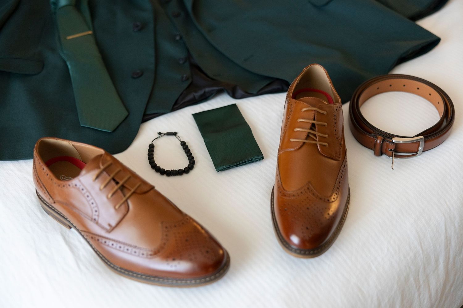 Brown leather dress shoes with brogue detailing displayed on a white surface against a dark background.