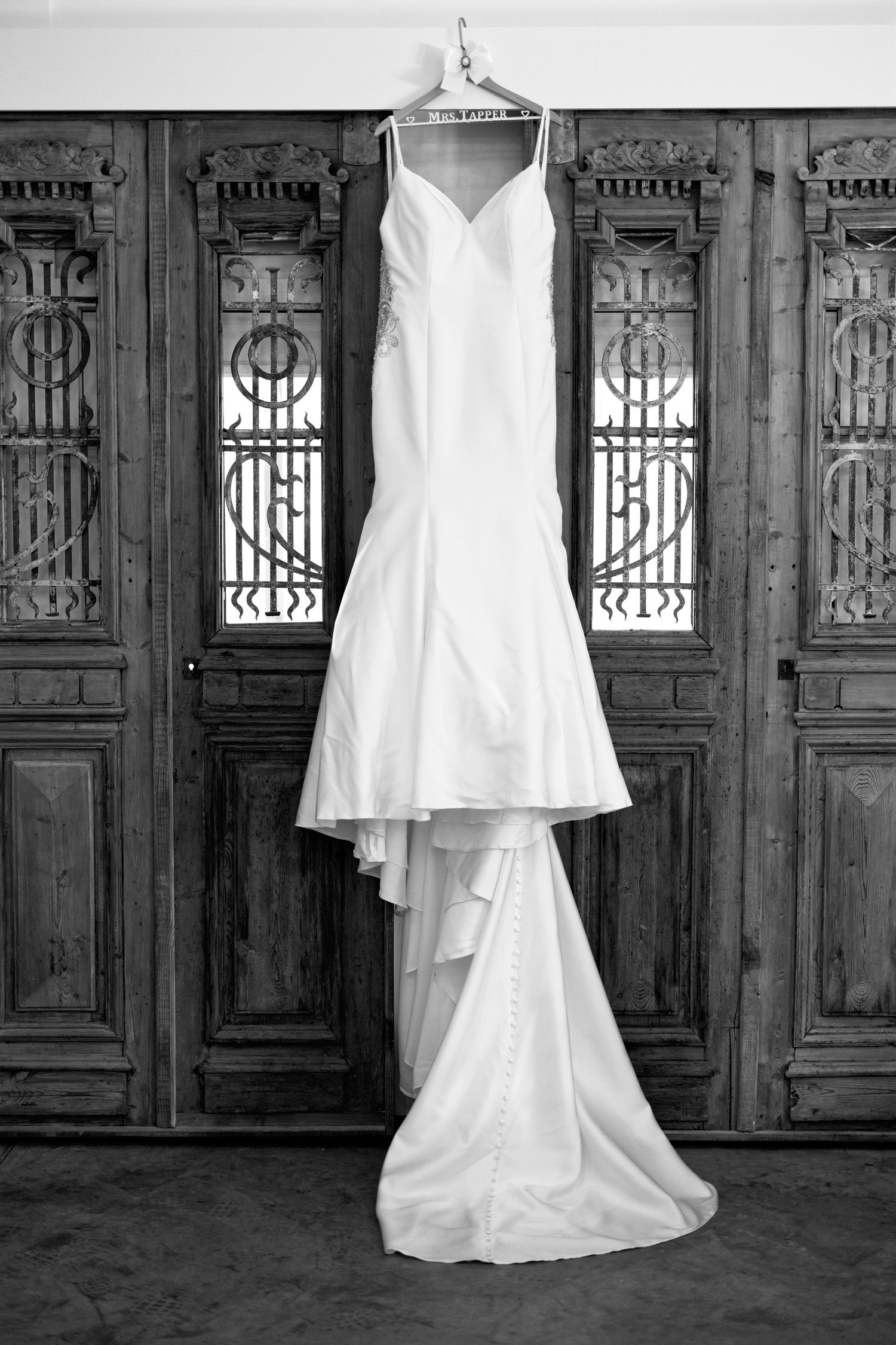 A series of black and white photos showing white wedding dresses displayed against ornate vintage wooden doors and panels.
