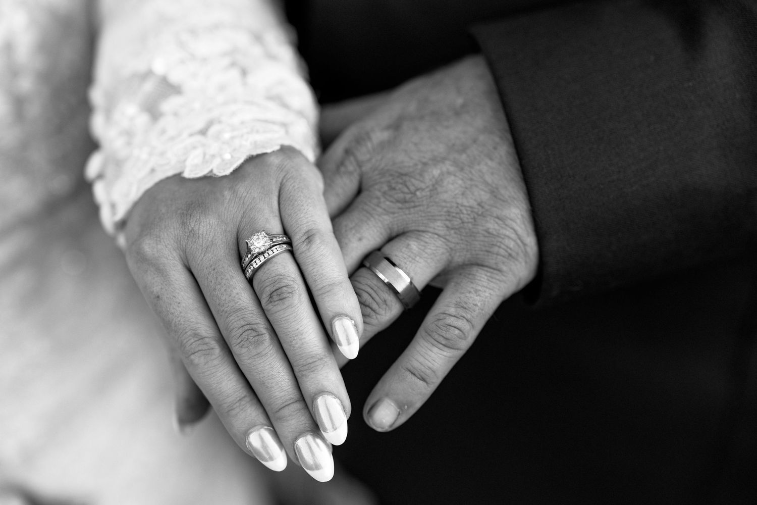 A close-up black and white photo of hands wearing wedding rings.