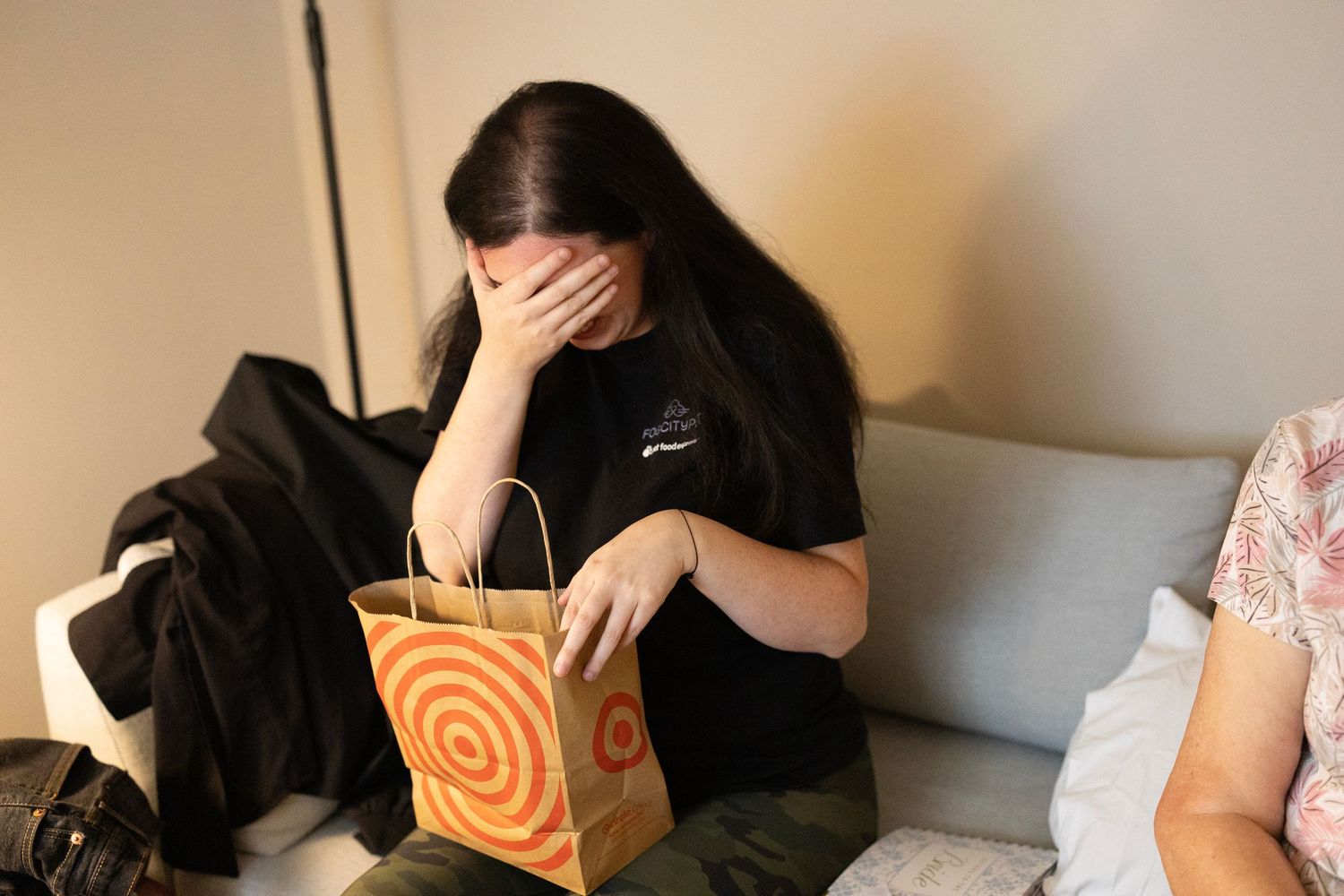 Woman covering her face with hand while holding a Target shopping bag, sitting on a couch indoors.
